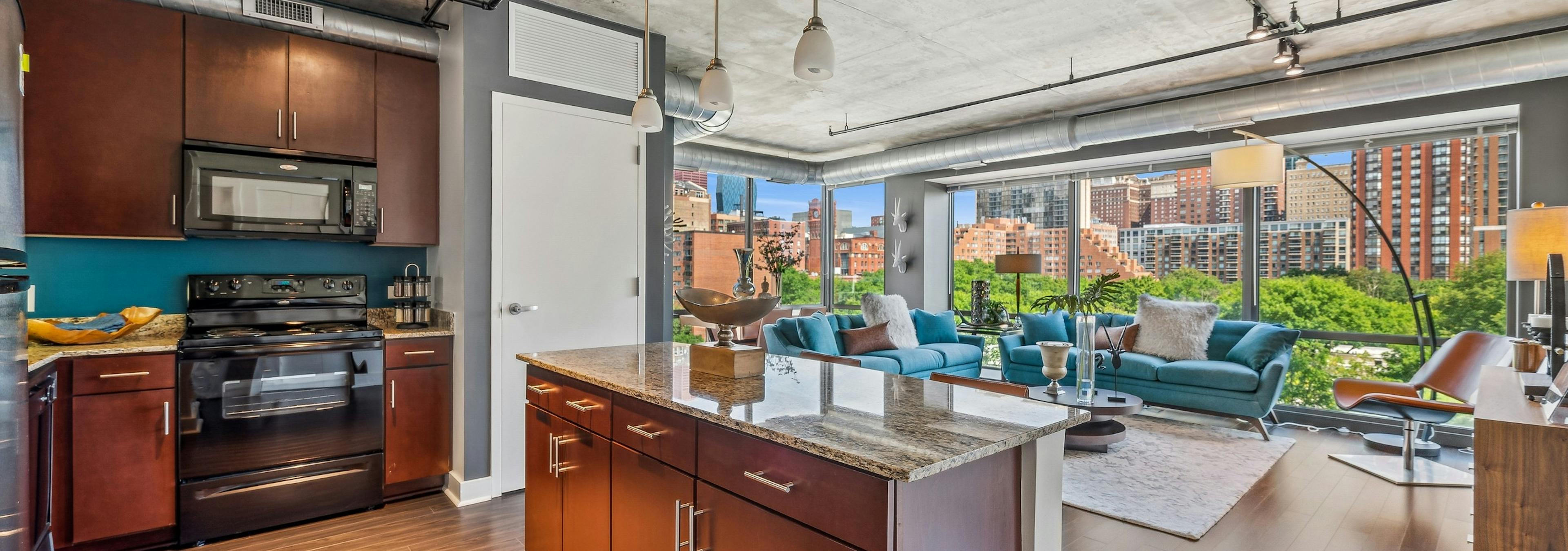 Kitchen with dark wood cabinets and granite countertops and living area with wall of windows  at AMLI 900 apartments