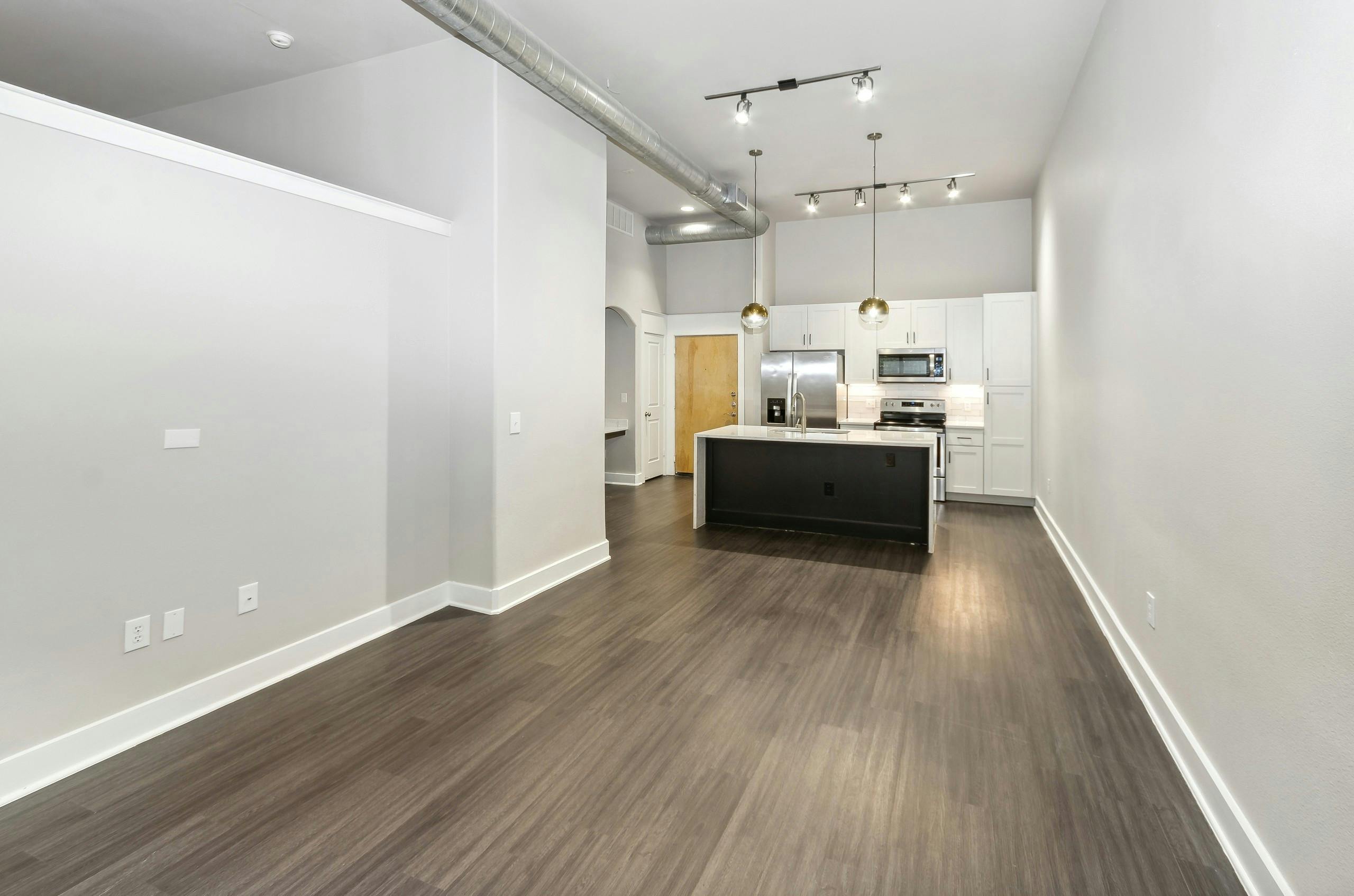 Living room and kitchen of remodeled AMLI Las Colinas apartment with white countertops and wood flooring