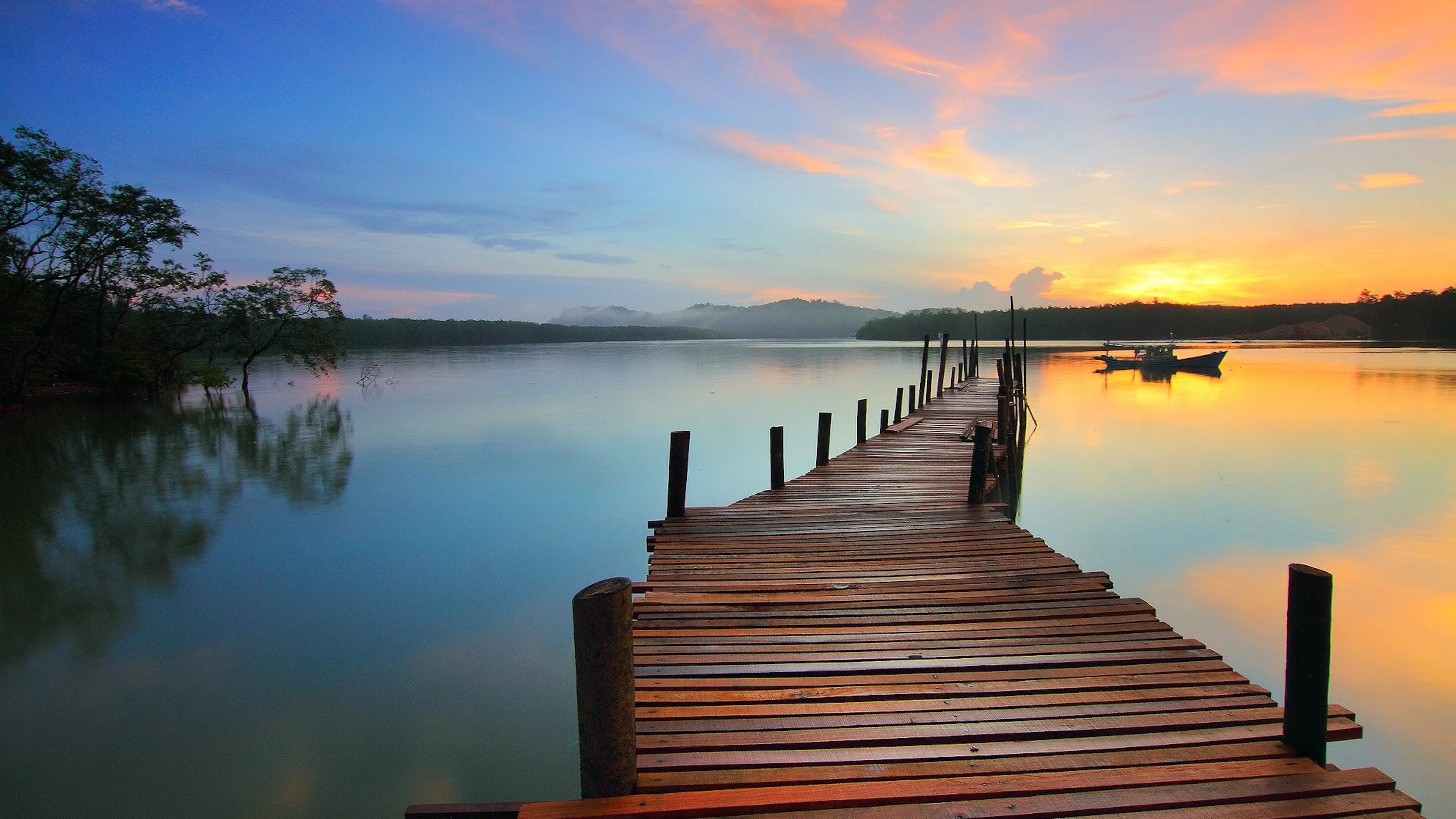 A long wooden pier stretching out into a big clear lake with reflections of sunrise in the water