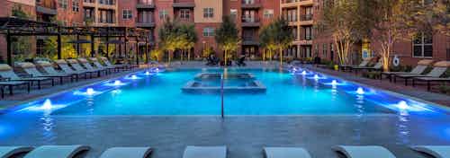 AMLI Grapevine swimming pool at dusk with pool lights and surrounded by green trees and light gray lounge seating