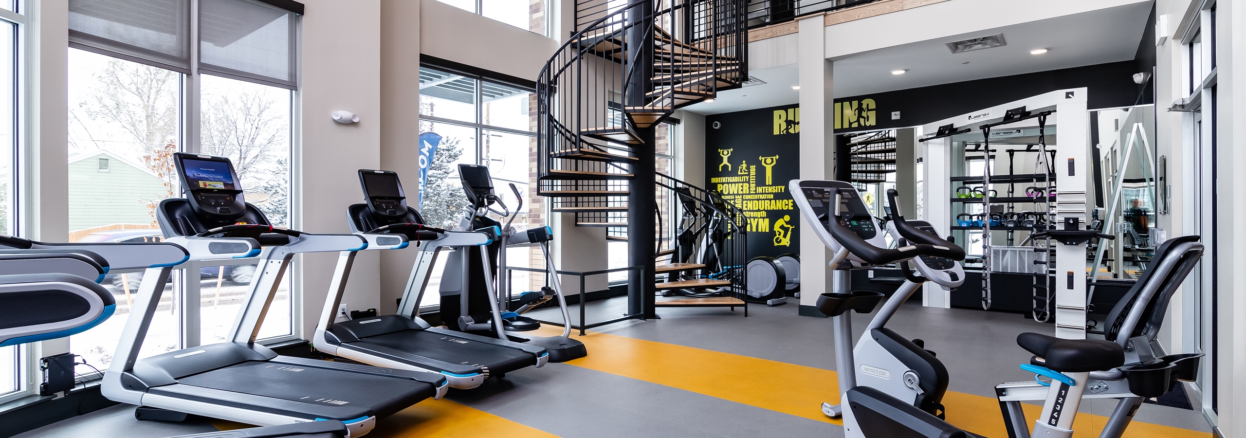 Fitness center at AMLI Littleton Village apartments with cardio machines, motion cage and spiral staircase to upper gym level