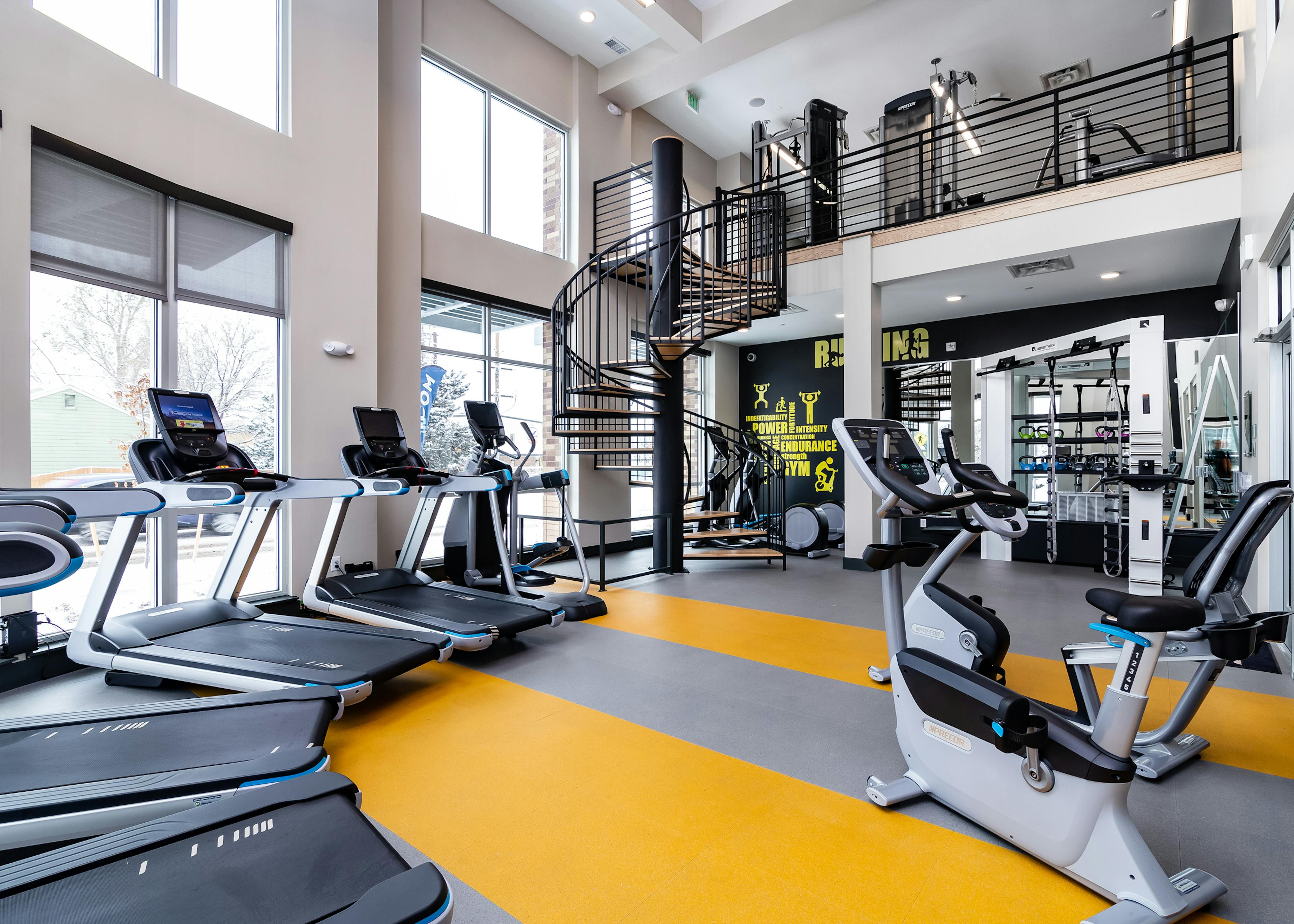 Fitness center at AMLI Littleton Village apartments with cardio machines, motion cage and spiral staircase to upper gym level