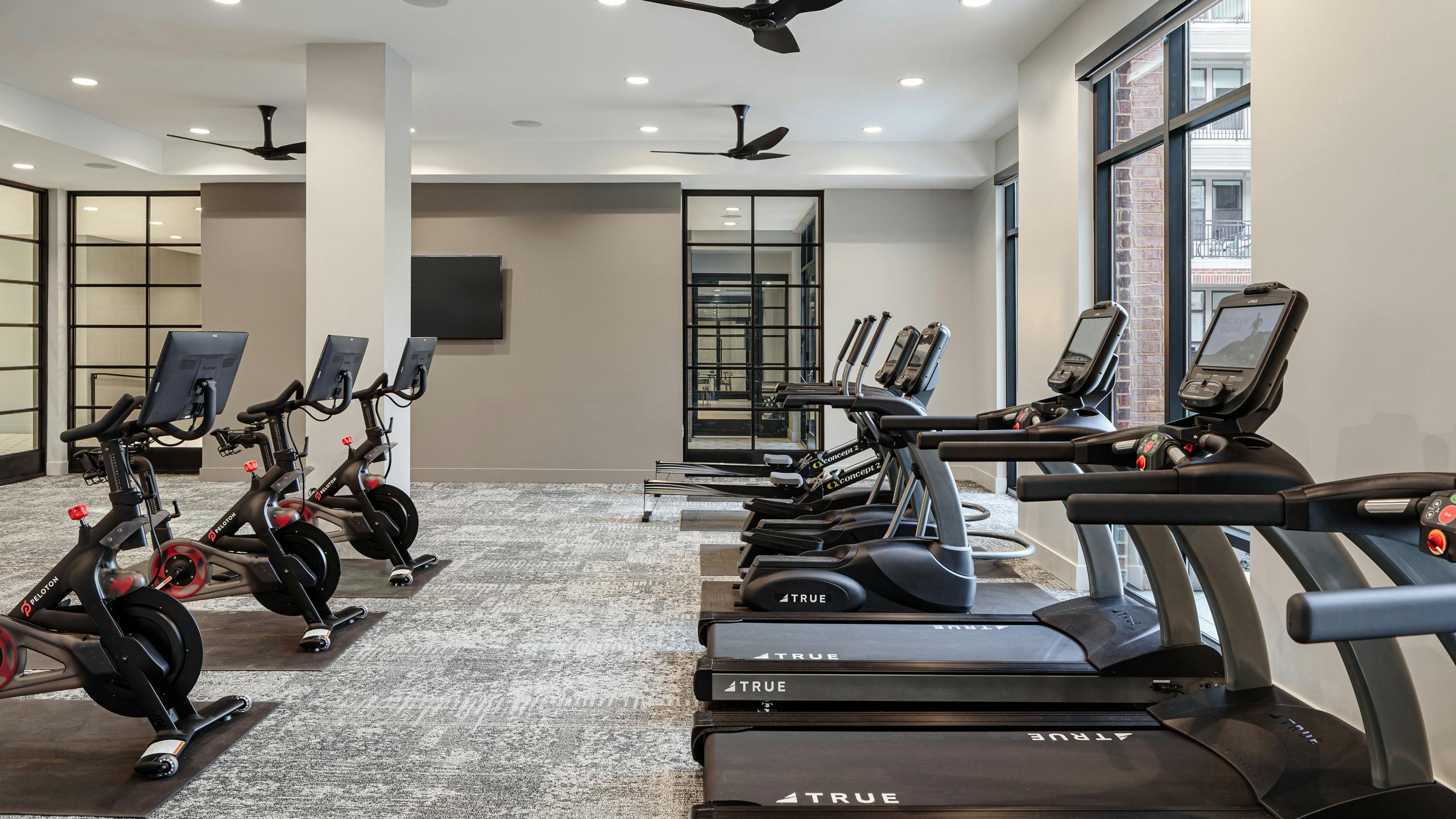 Interior of fitness center at AMLI Addison with treadmills facing large windows and exercise bikes in the row behind