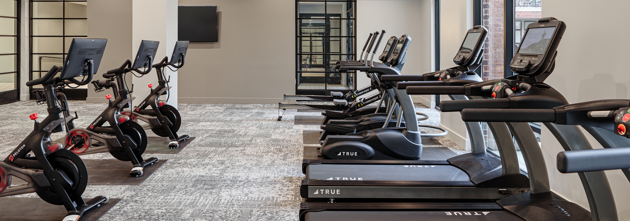 Interior of fitness center at AMLI Addison with treadmills facing large windows and exercise bikes in the row behind