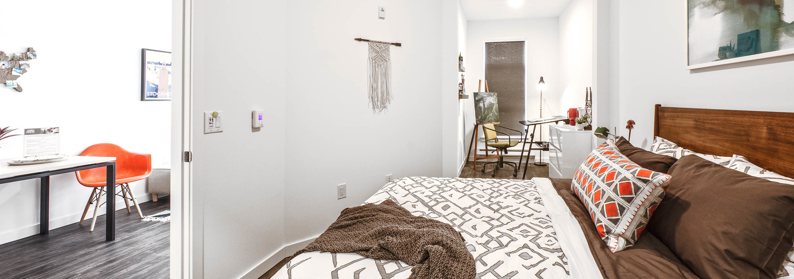 View of a bedroom of a AMLI Wallingford apartment with queen size bed large window and slight view of the kitchen living room