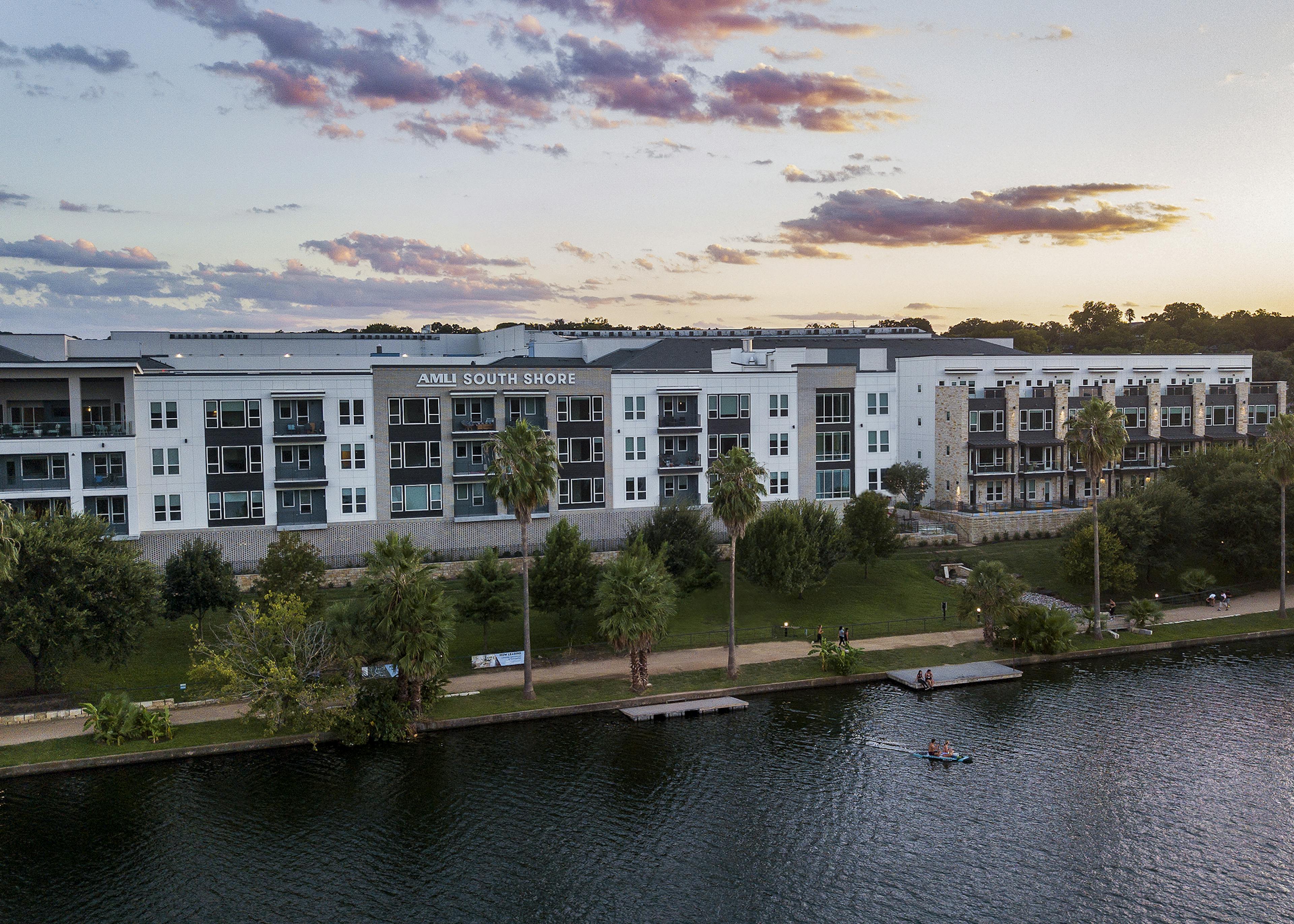 An aerial view at sunset of AMLI South Shore exterior façade with people kayaking in the lake and enjoying the walking trail