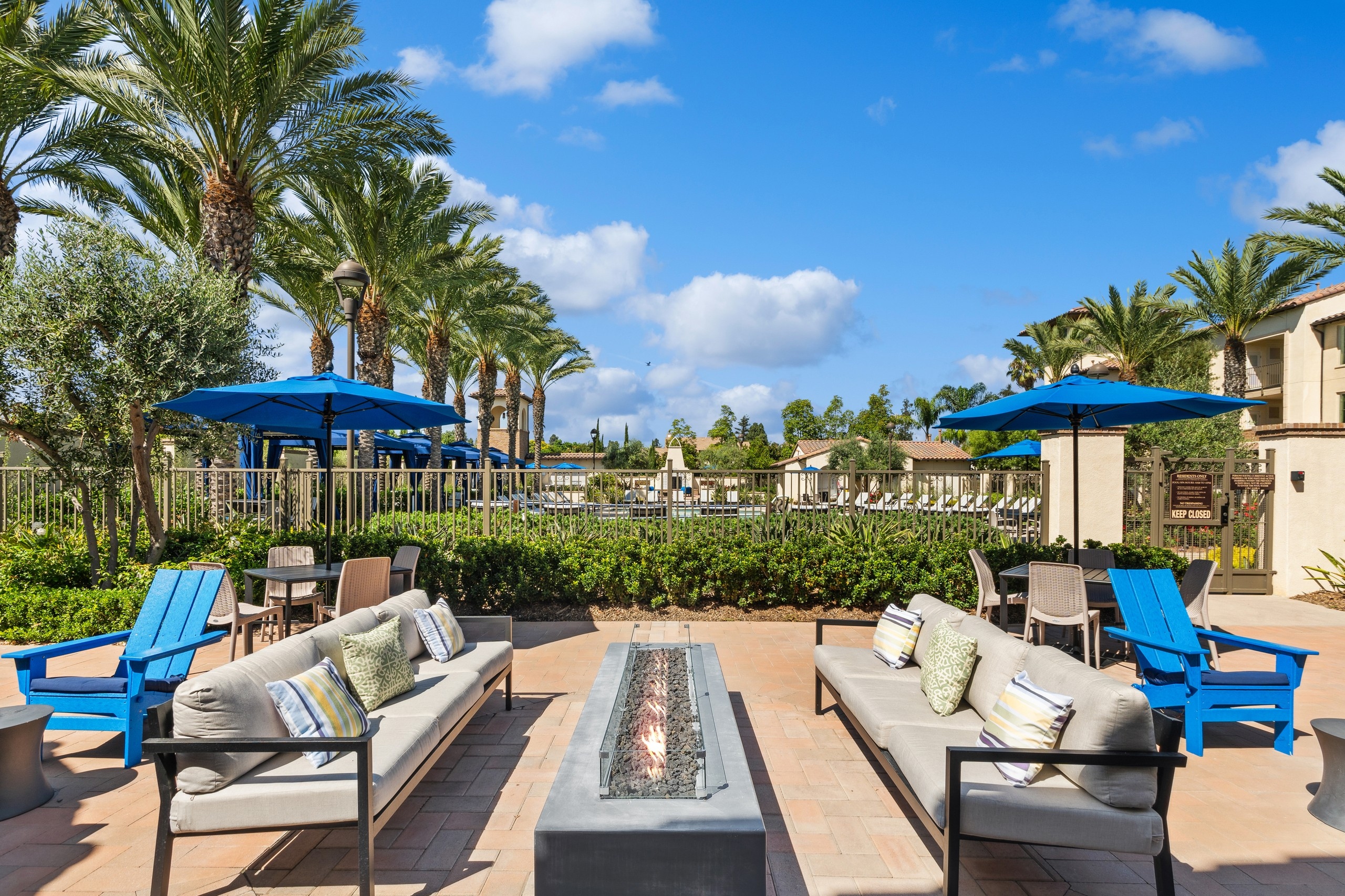 Exterior view of couch and Adirondack seating at AMLI Spanish Hills surrounding a long lit firepit next to the pool fence