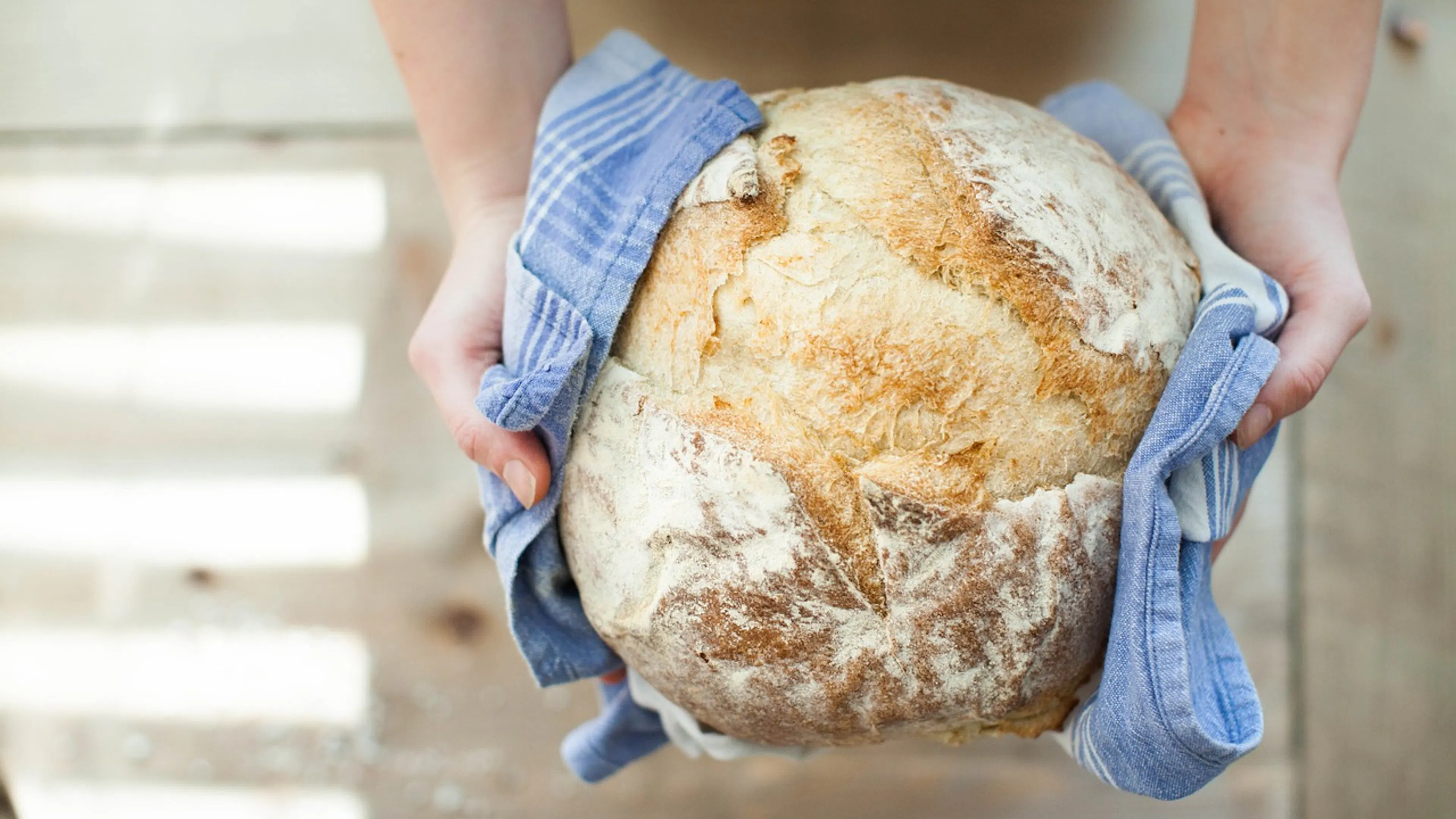 A round loaf of fresh homemade bread wrapped in a blue kitchen towel