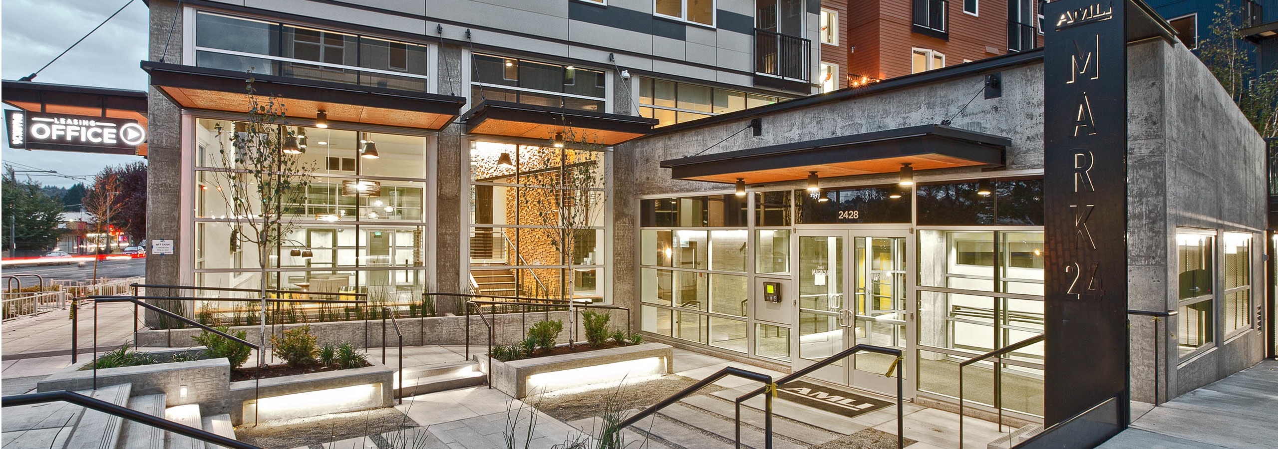 Exterior of AMLI Mark24 apartment community entrance at dusk with view of lobby and leasing office and sidewalk and street