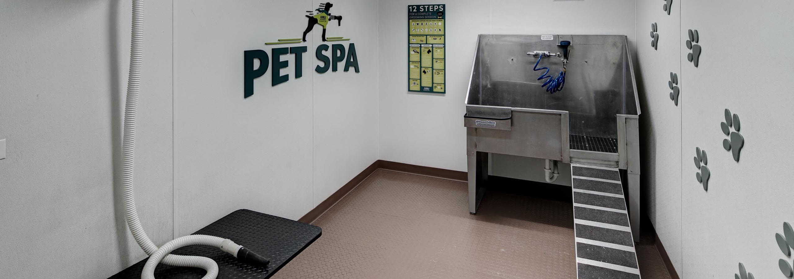 AMLI Evanston pet spa with large stainless steel tub and a hair vacuum hose featuring paw print decals along the wall