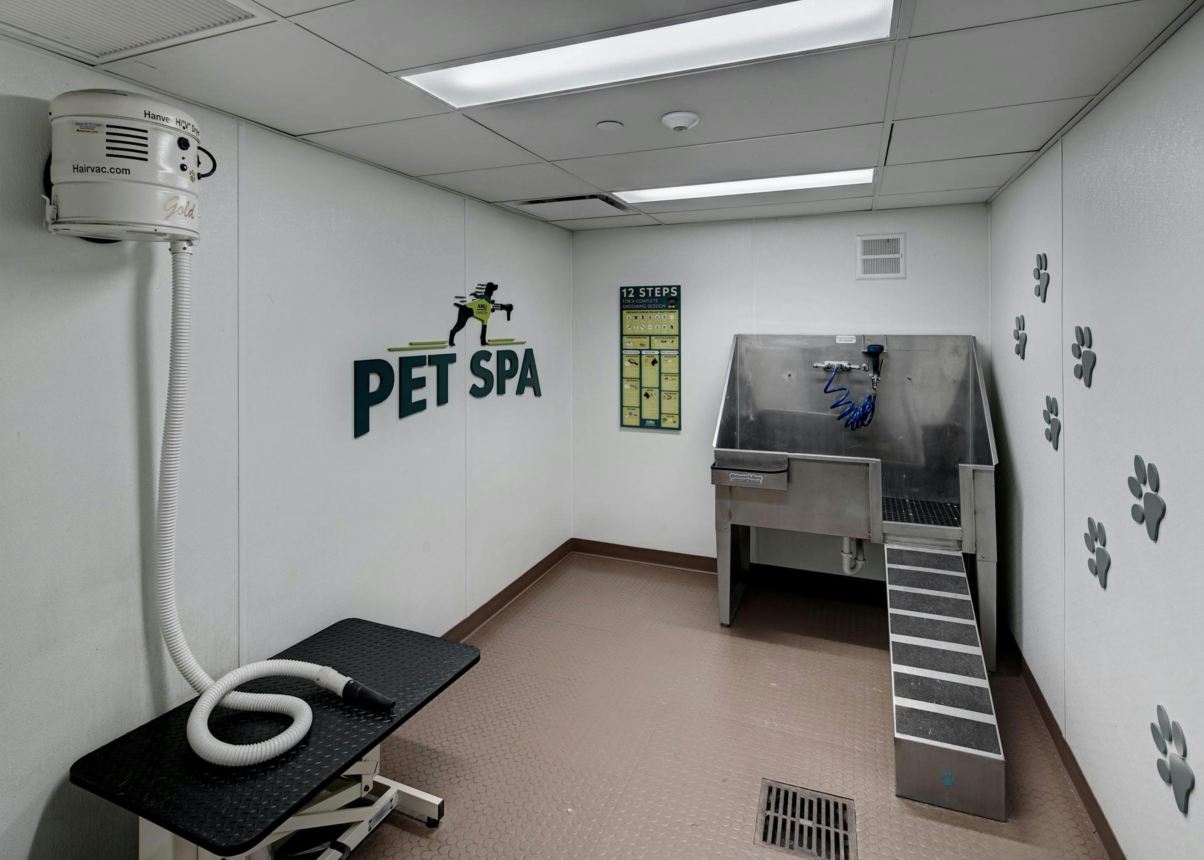 AMLI Evanston pet spa with large stainless steel tub and a hair vacuum hose featuring paw print decals along the wall 