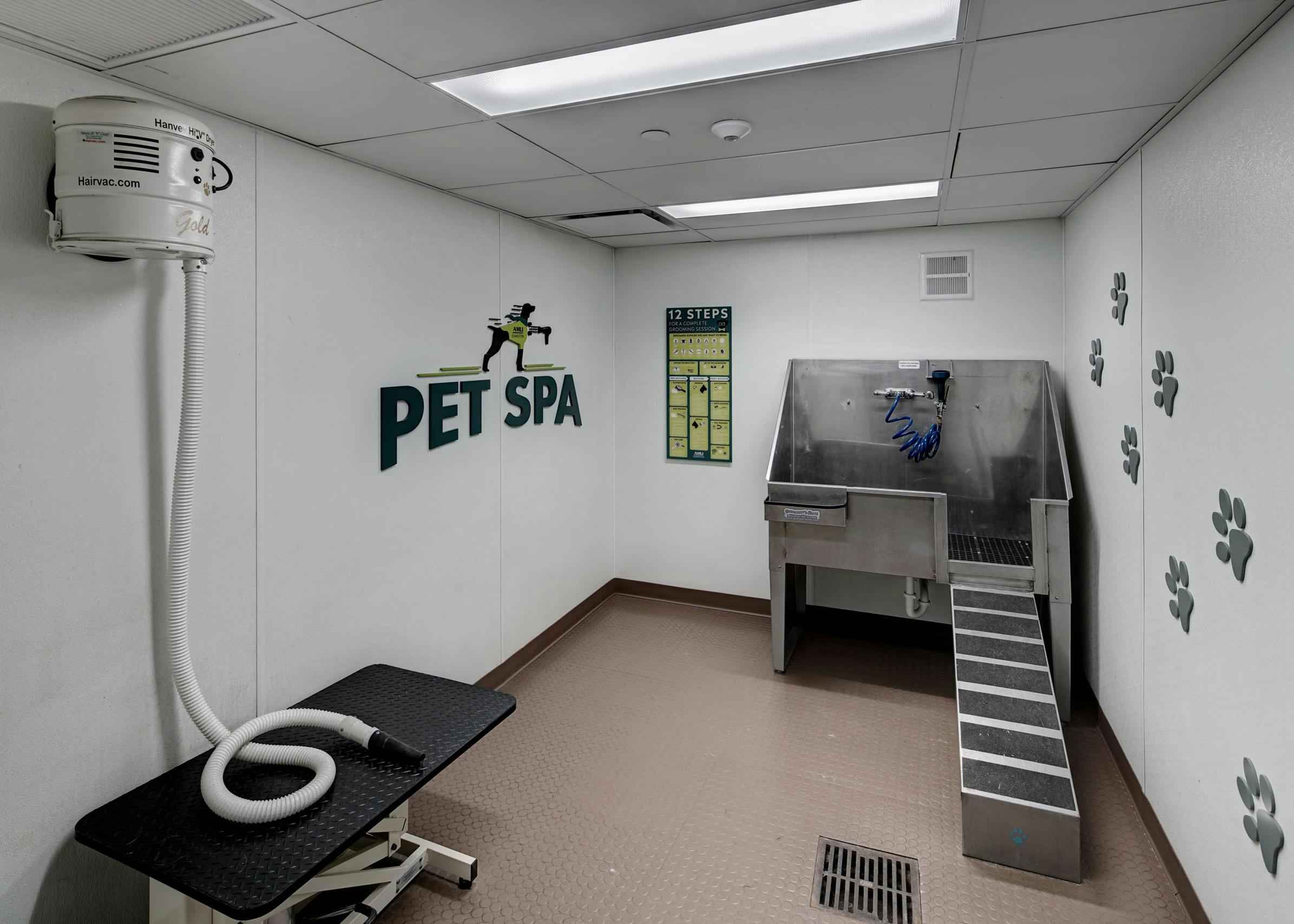 AMLI Evanston pet spa with large stainless steel tub and a hair vacuum hose featuring paw print decals along the wall