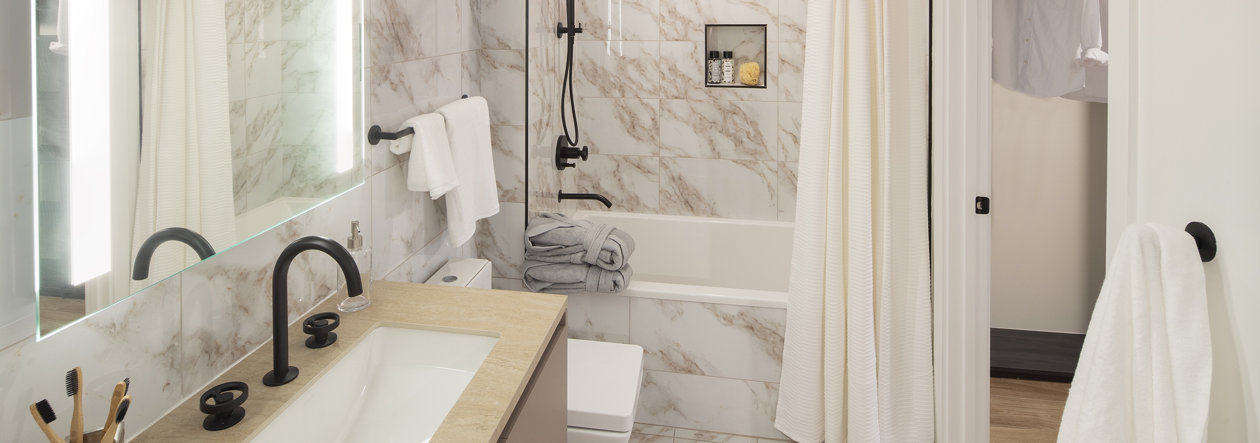AMLI Midtown Miami apartment bathroom with marble floors and soaking tub with marble surround and vanity with backlit mirror