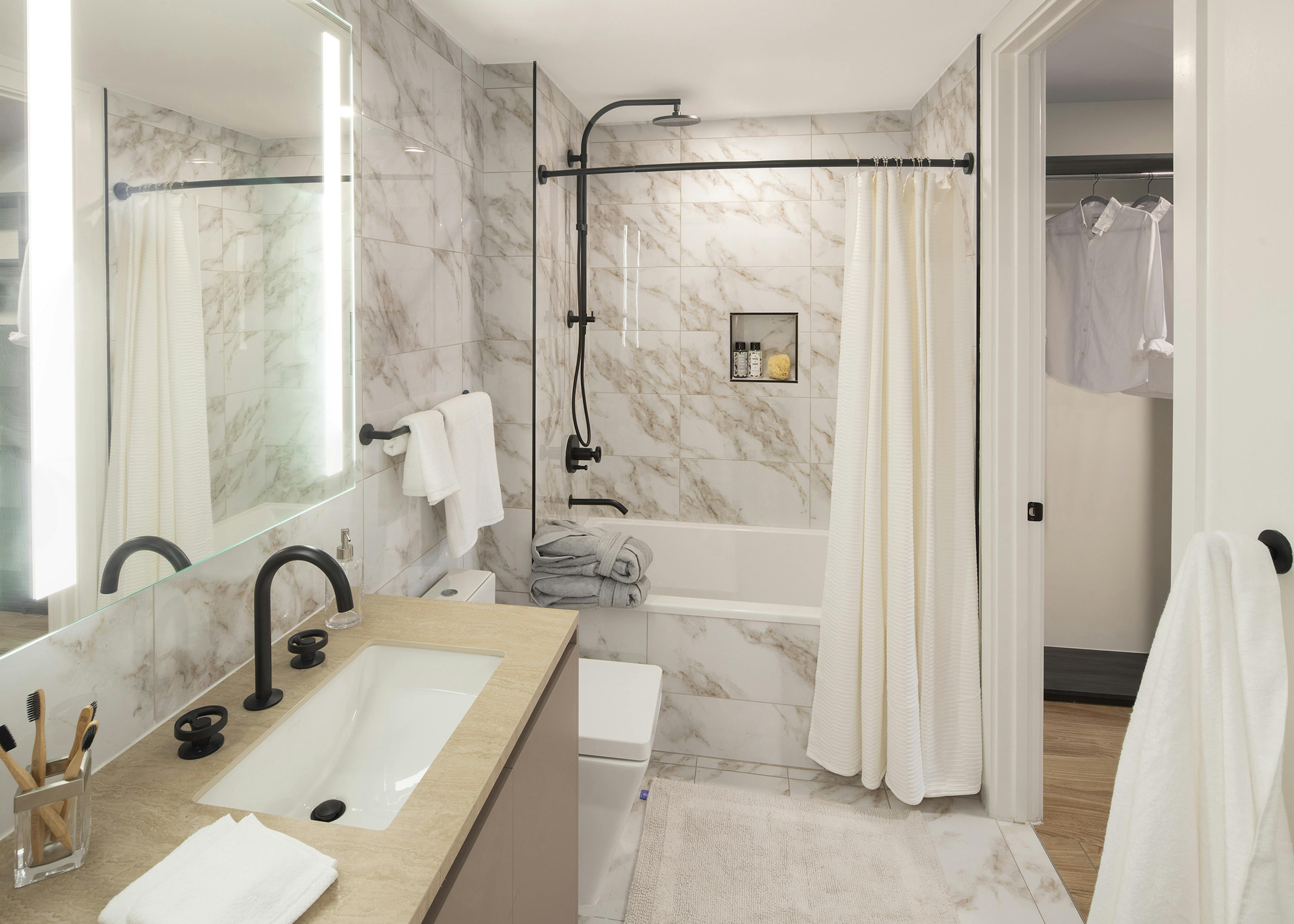 AMLI Midtown Miami apartment bathroom with marble floors and soaking tub with marble surround and vanity with backlit mirror 