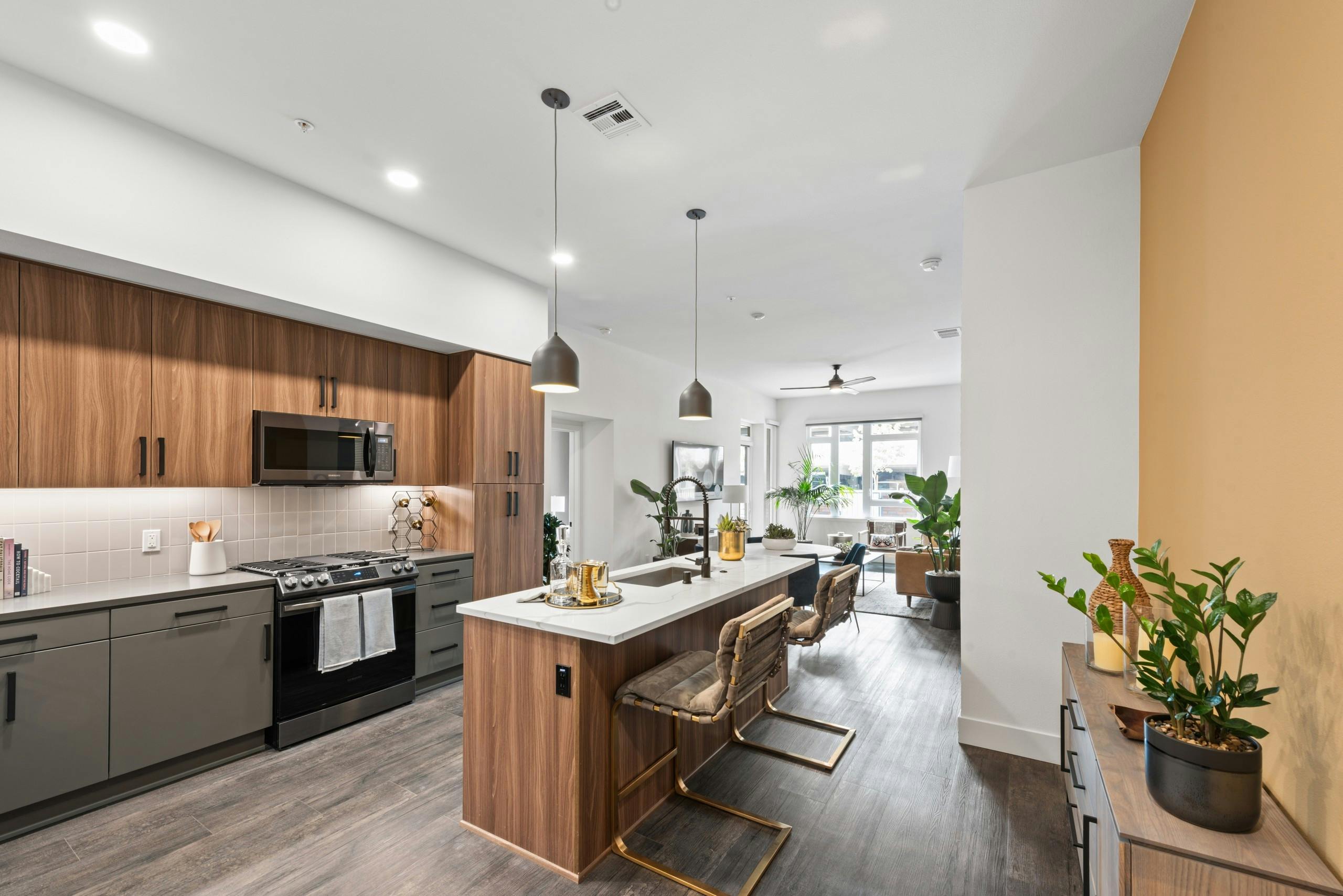 Interior of AMLI Old Pasadena apartment kitchen with quartz countertop looking into furnished living room with ceiling fan