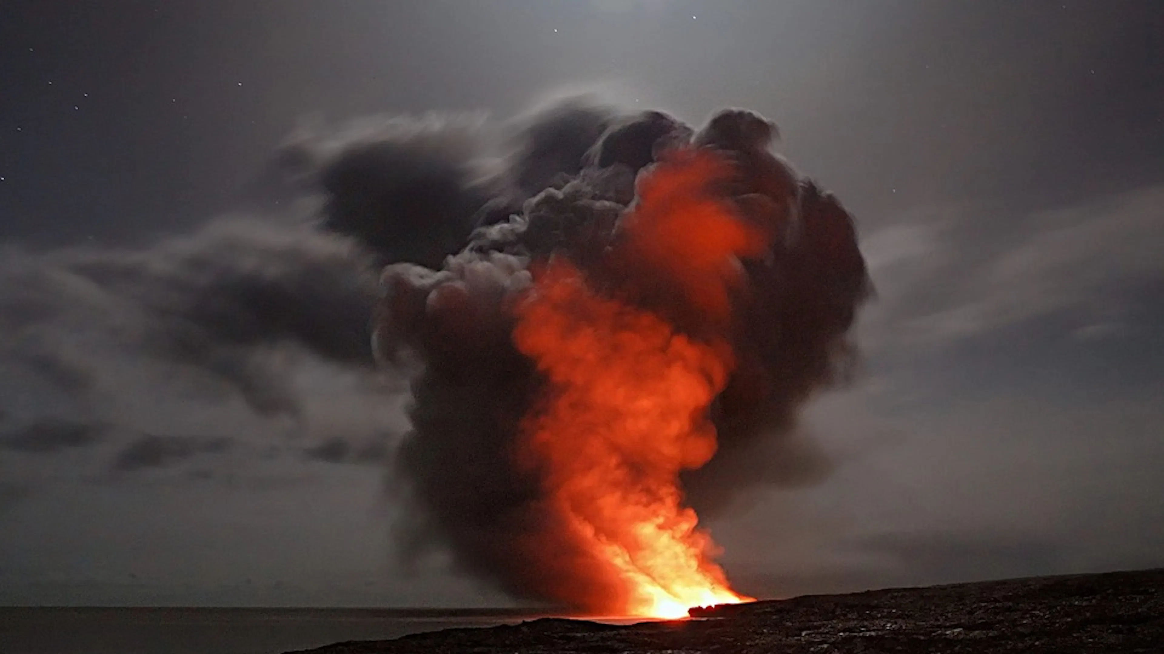 A volcano spewing magma and smoke out of the ocean into the night sky