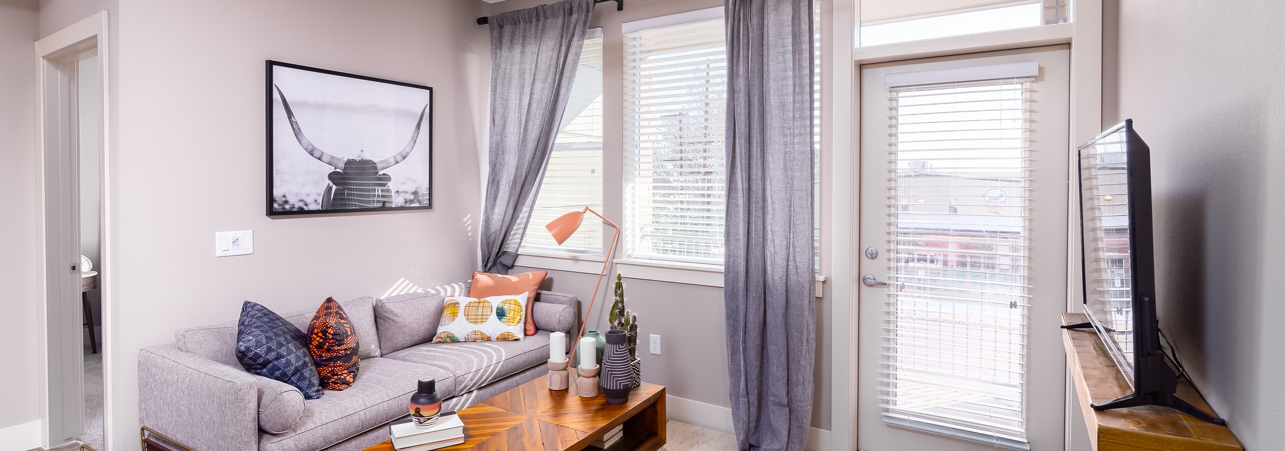 Interior daytime view of AMLI Littleton Village apartment living room with gray cozy couch, coffee table and big screen TV