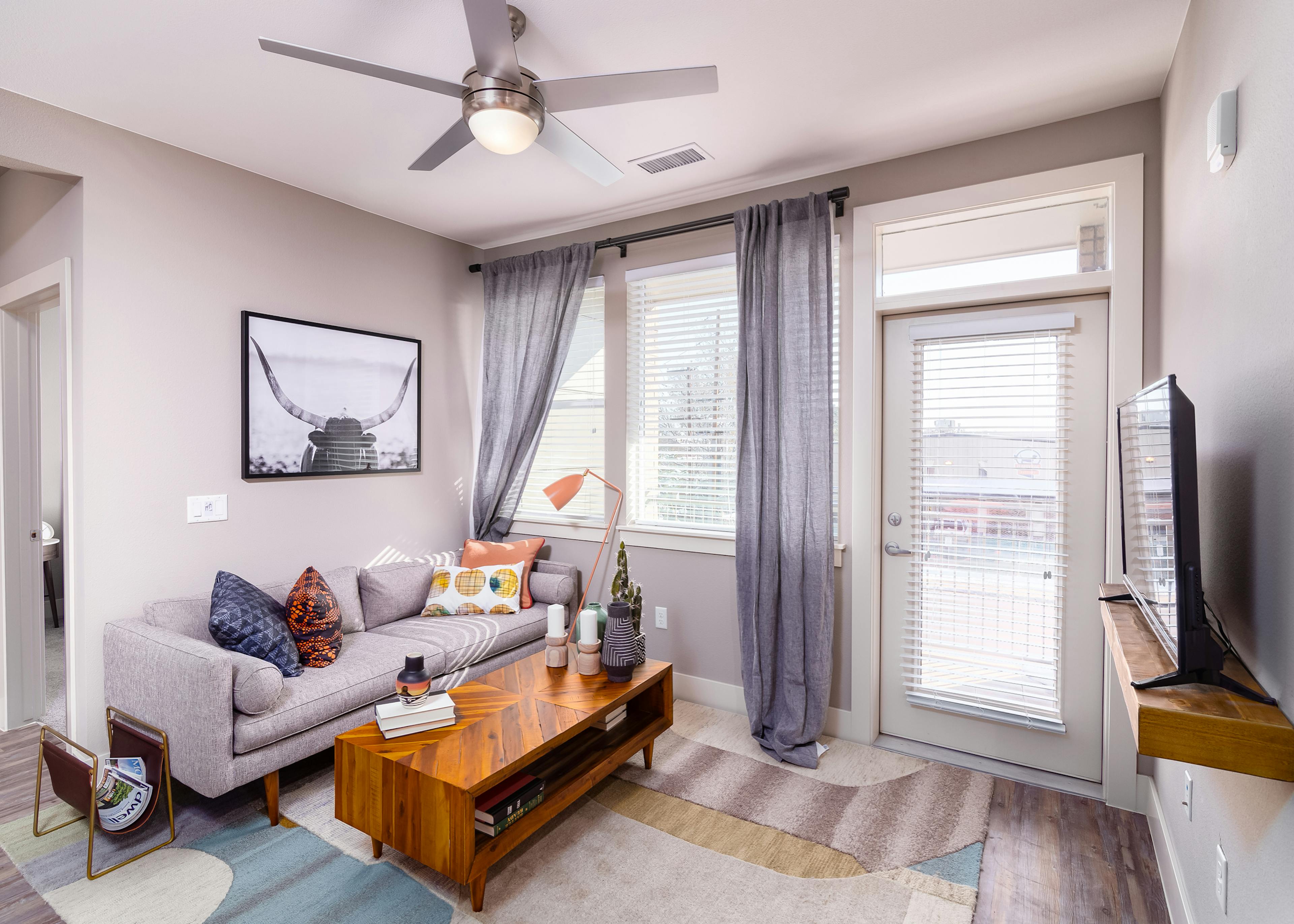 Interior daytime view of AMLI Littleton Village apartment living room with gray cozy couch, coffee table and big screen TV