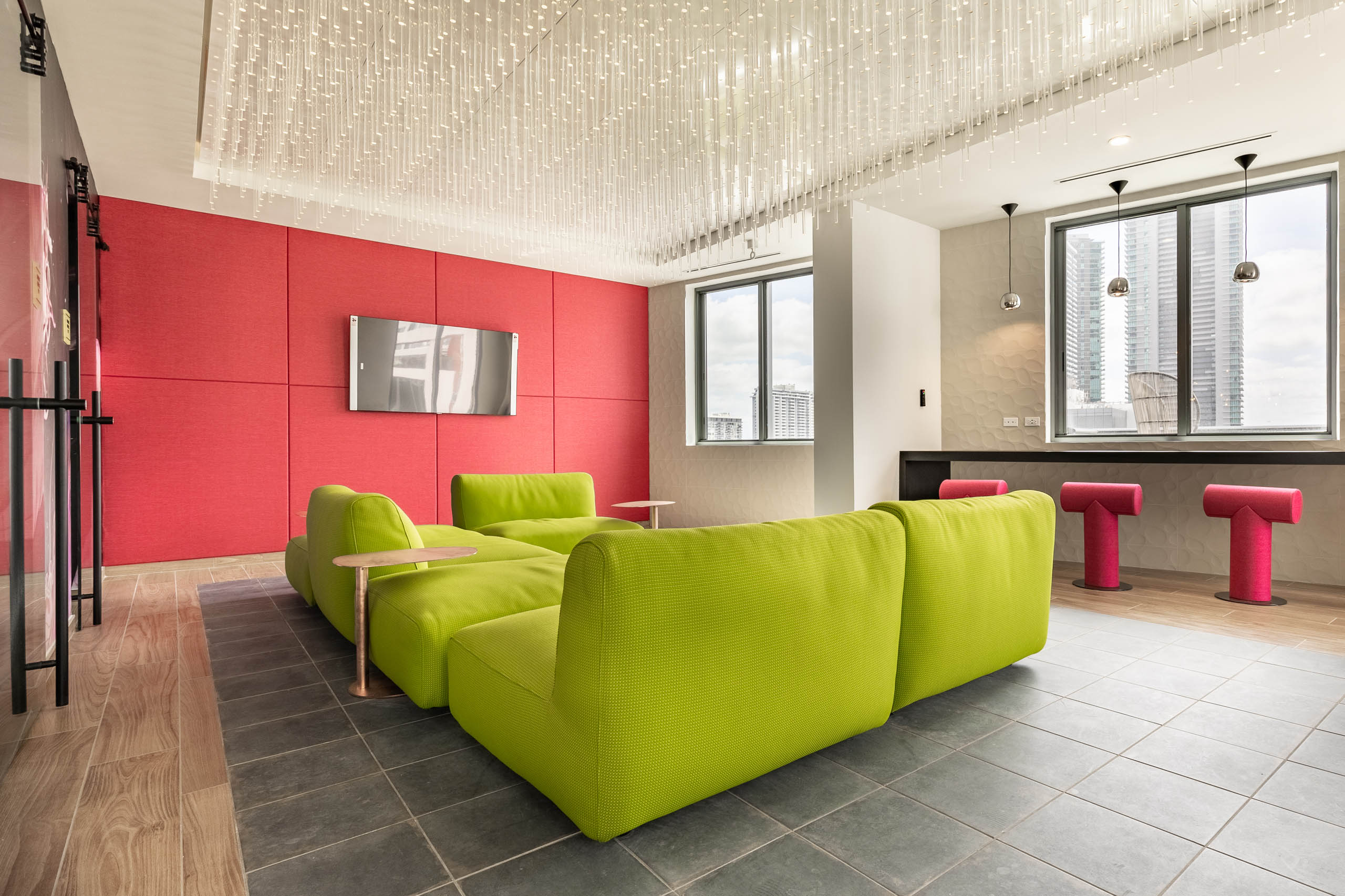 AMLI Midtown Miami apartments social club with bright green modern sofa and red panel wall with TV and crystal light fixture 