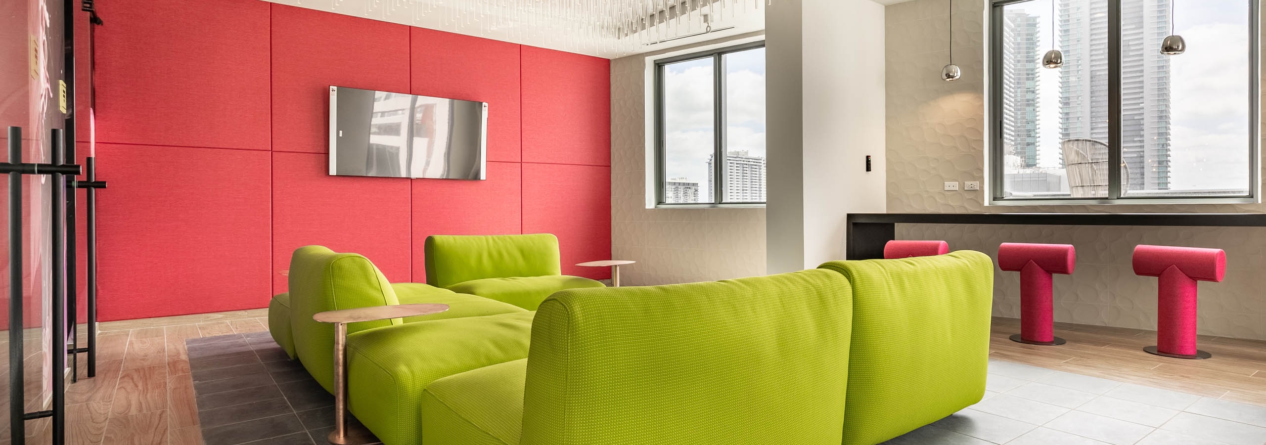 AMLI Midtown Miami apartments social club with bright green modern sofa and red panel wall with TV and crystal light fixture