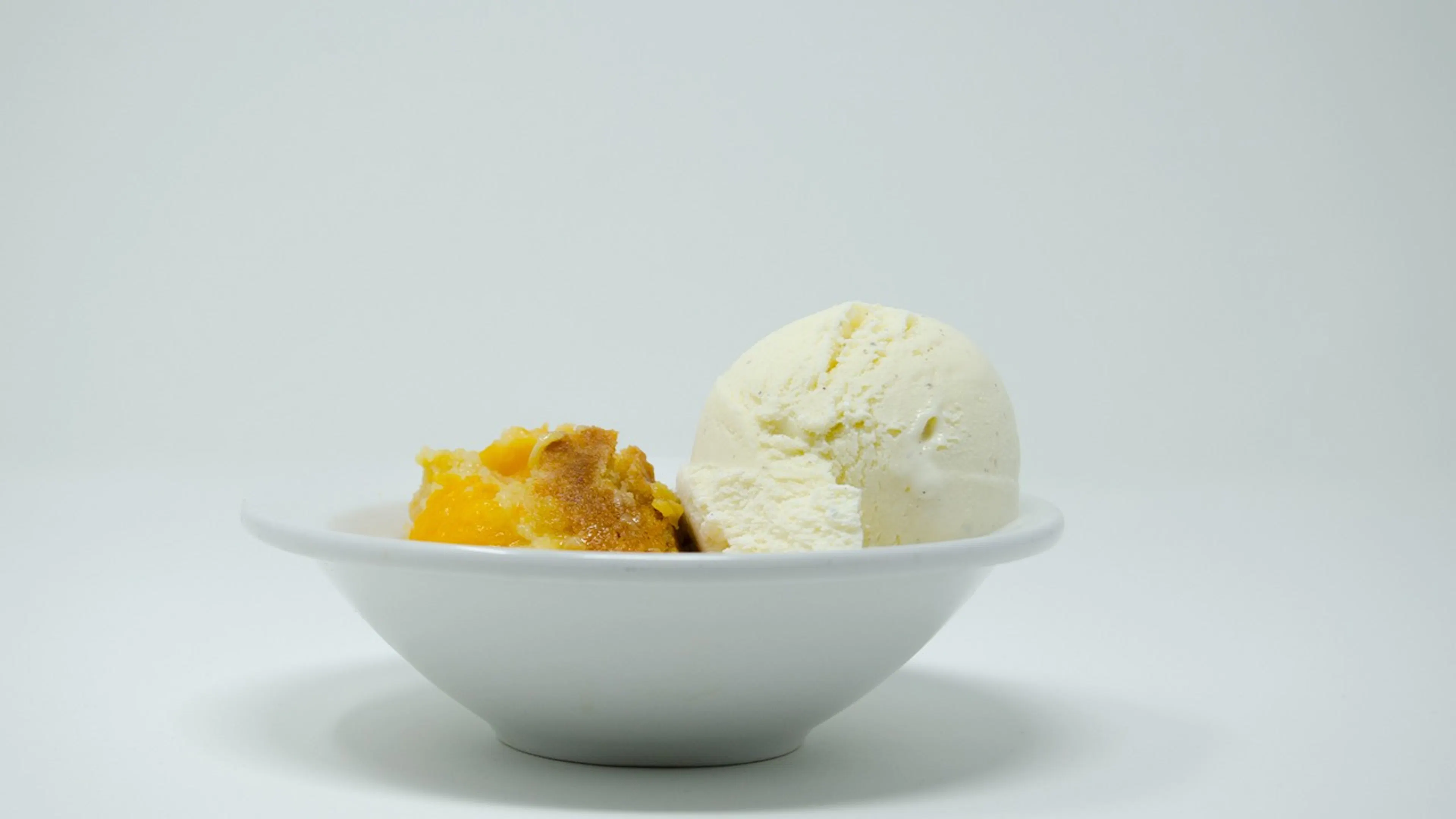 A white ceramic bowl with peach cobbler and a scoop of vanilla ice cream