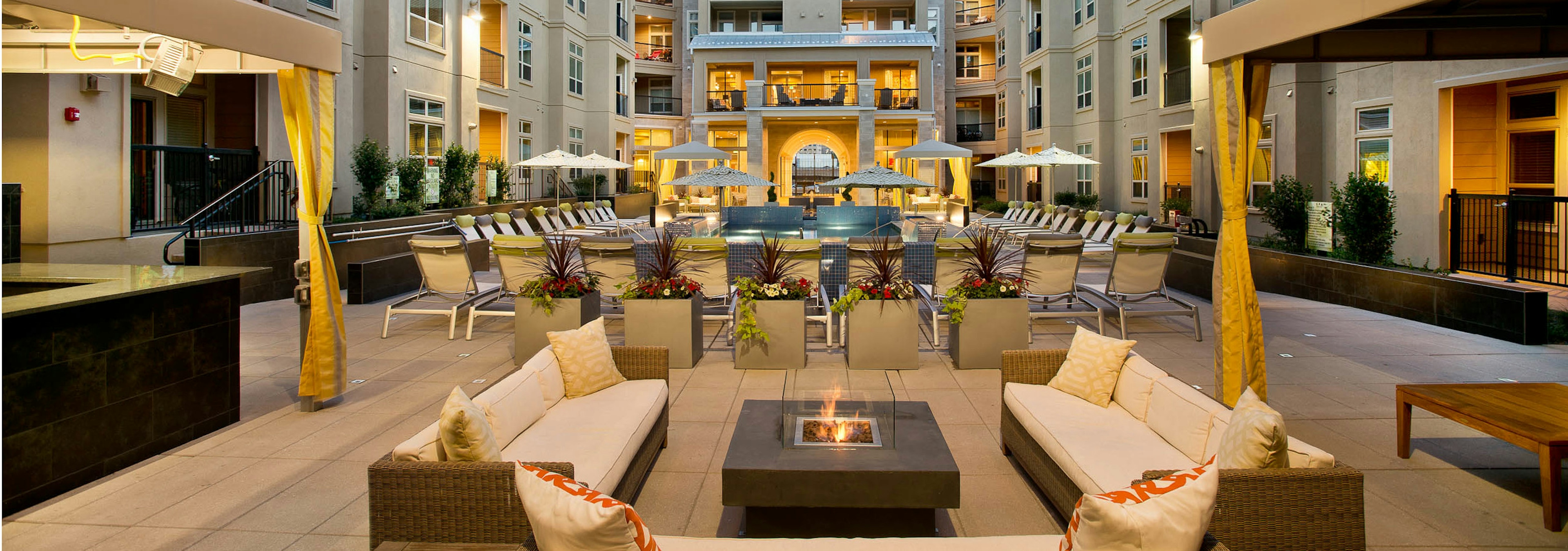 Dusk exterior view of AMLI RidgeGate pool area with cabanas, fire pit and planters with flowers facing grand library terrace