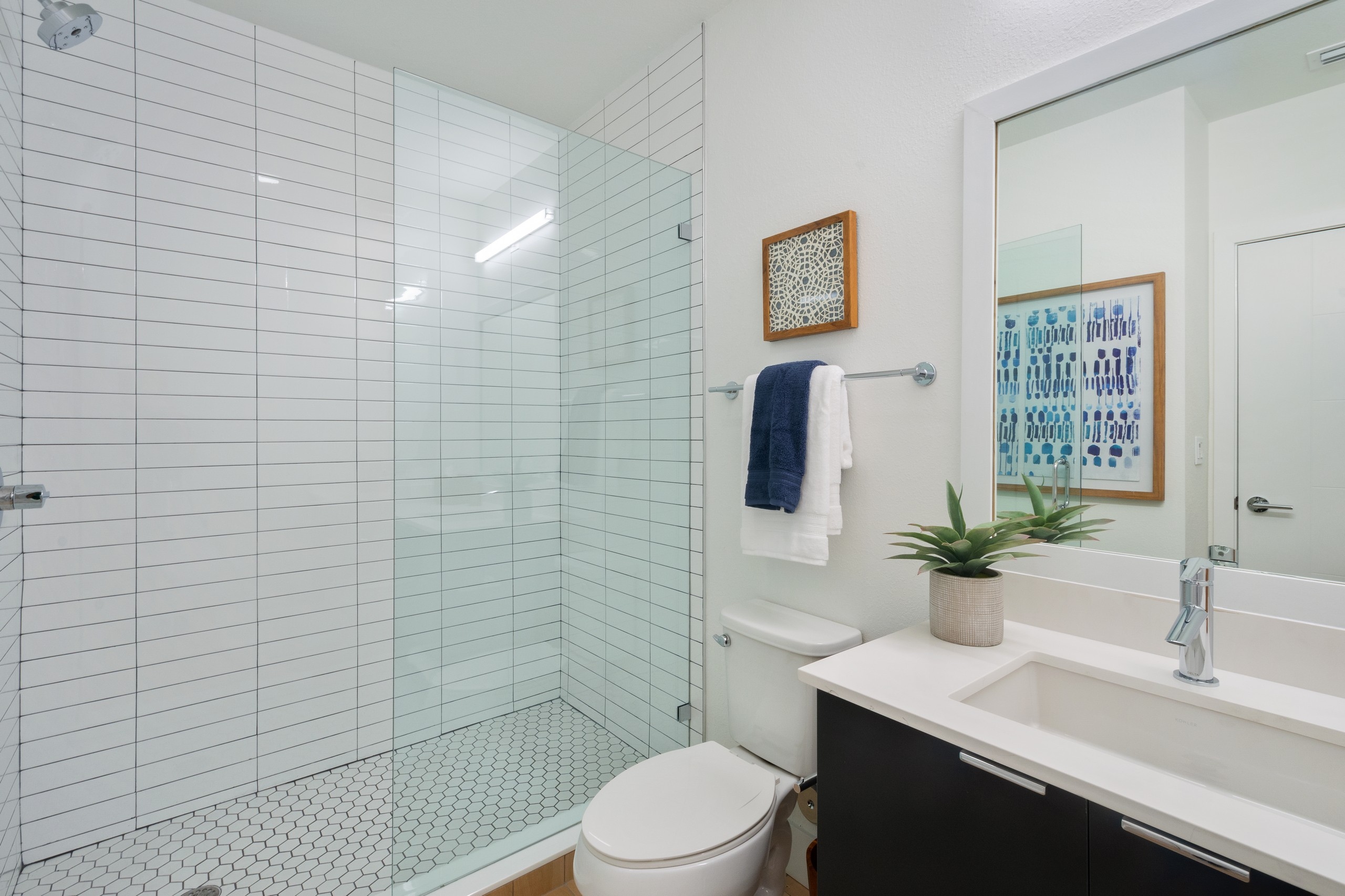 AMLI Park West bathroom with wood vanity and white quartz counter with mirror above and glass shower enclosure with tile 