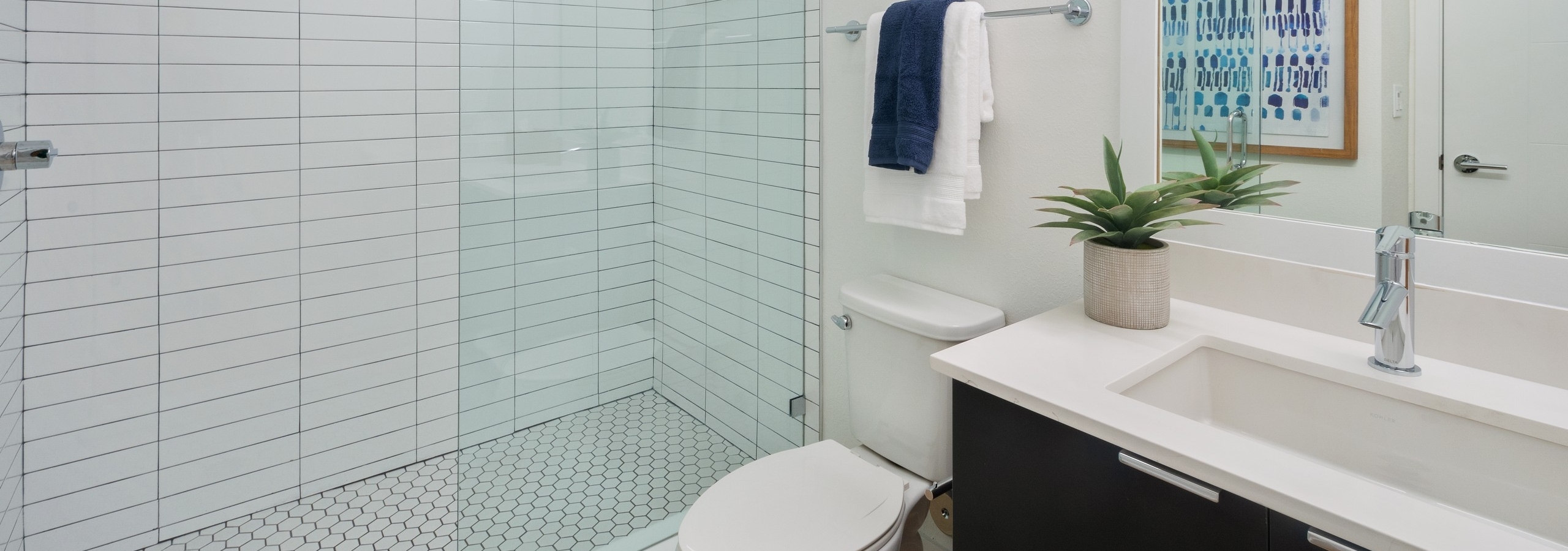 AMLI Park West bathroom with wood vanity and white quartz counter with mirror above and glass shower enclosure with tile