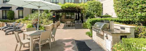 Daytime view of AMLI Las Colinas grilling station with shaded dining area under a black canopy covered in lush greenery
