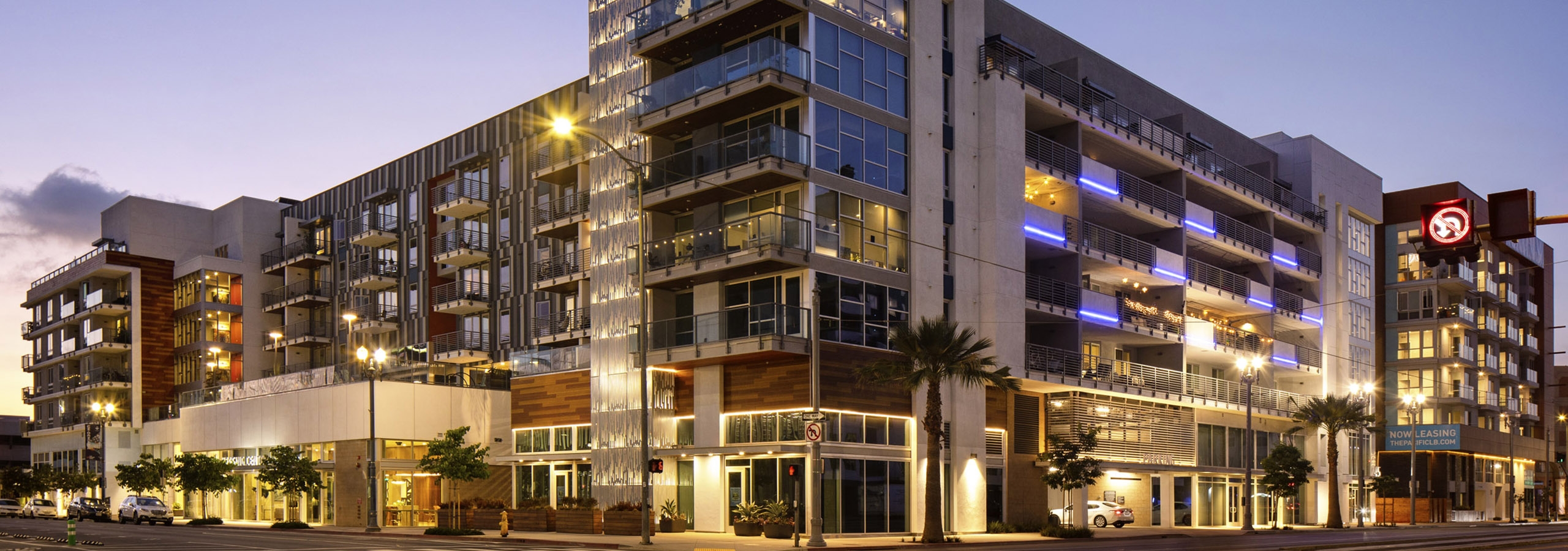 AMLI Park Broadway apartment building’s main tower lit up at dusk and surrounded by planters and trees along sidewalk