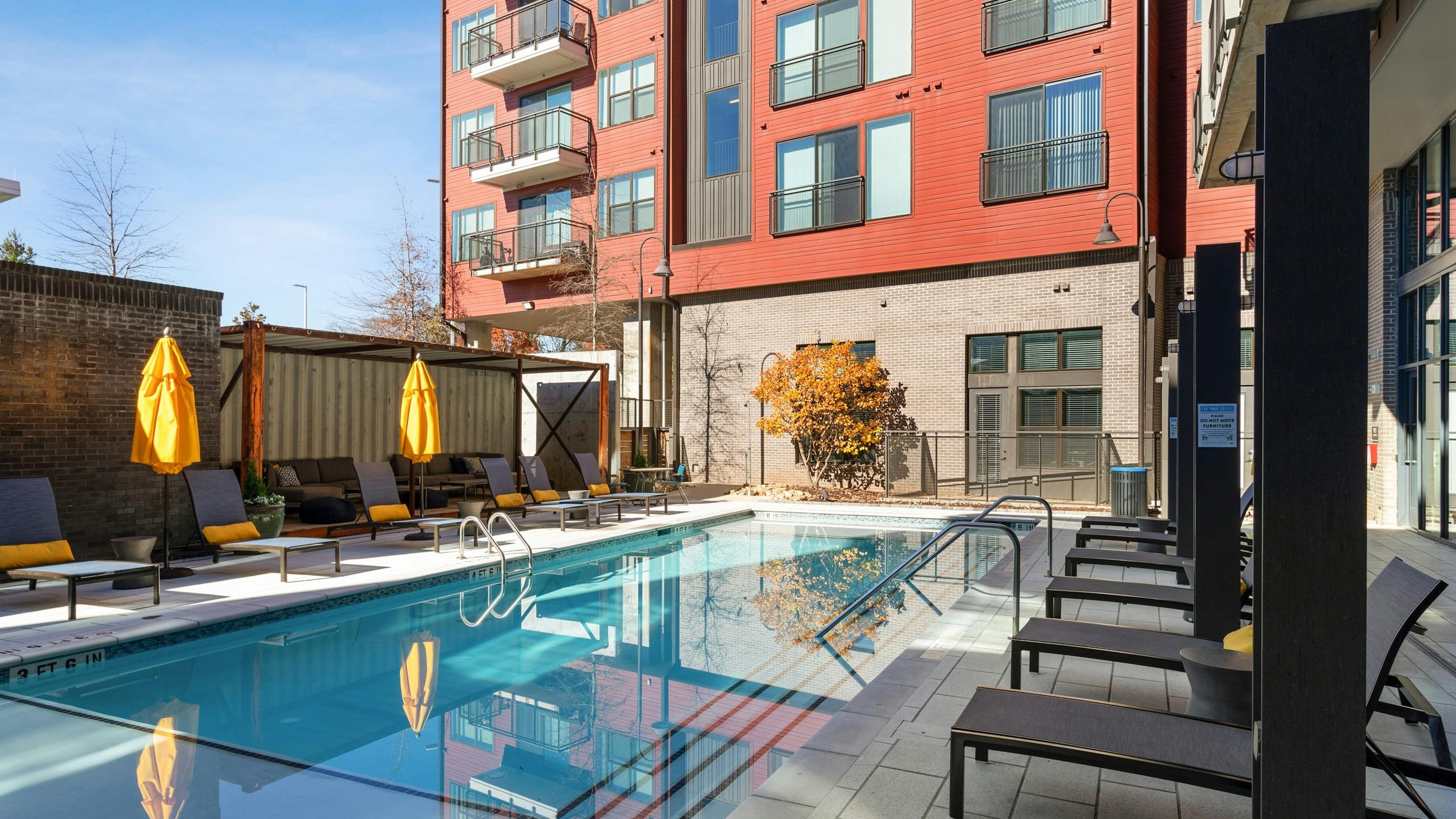 Sunny view of clear salt water pool at AMLI Westside apartments with several lounge seating arrangements and yellow umbrellas