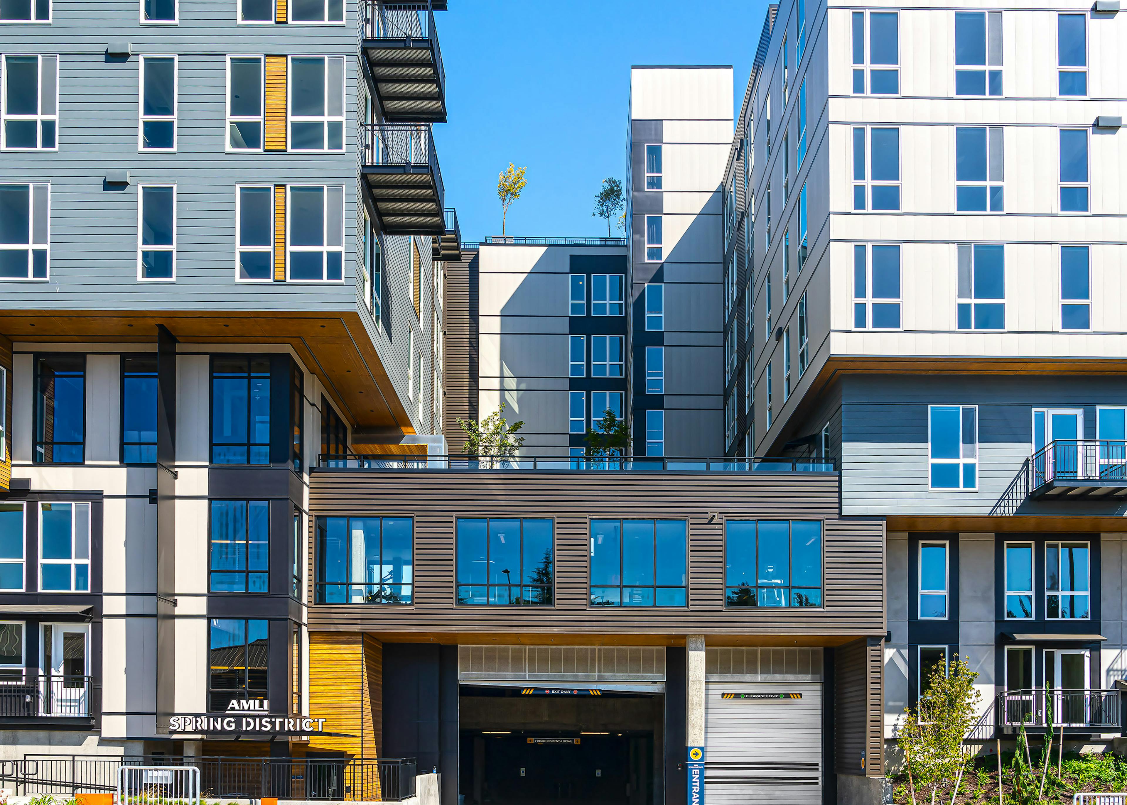 Blue and white and brown AMLI Spring District apartment building with logo sign and garage entrance and roof deck above