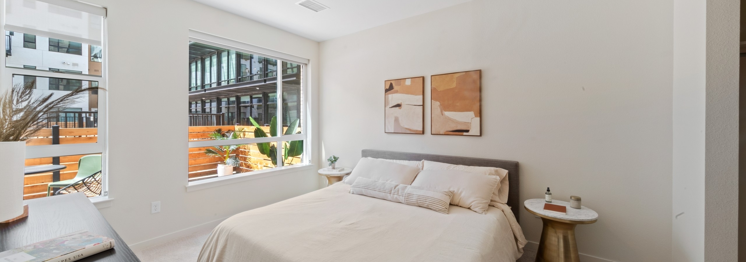 Bedroom at AMLI Broadway Park apartments with a queen size bed and a 2 large windows with a view out to the patio