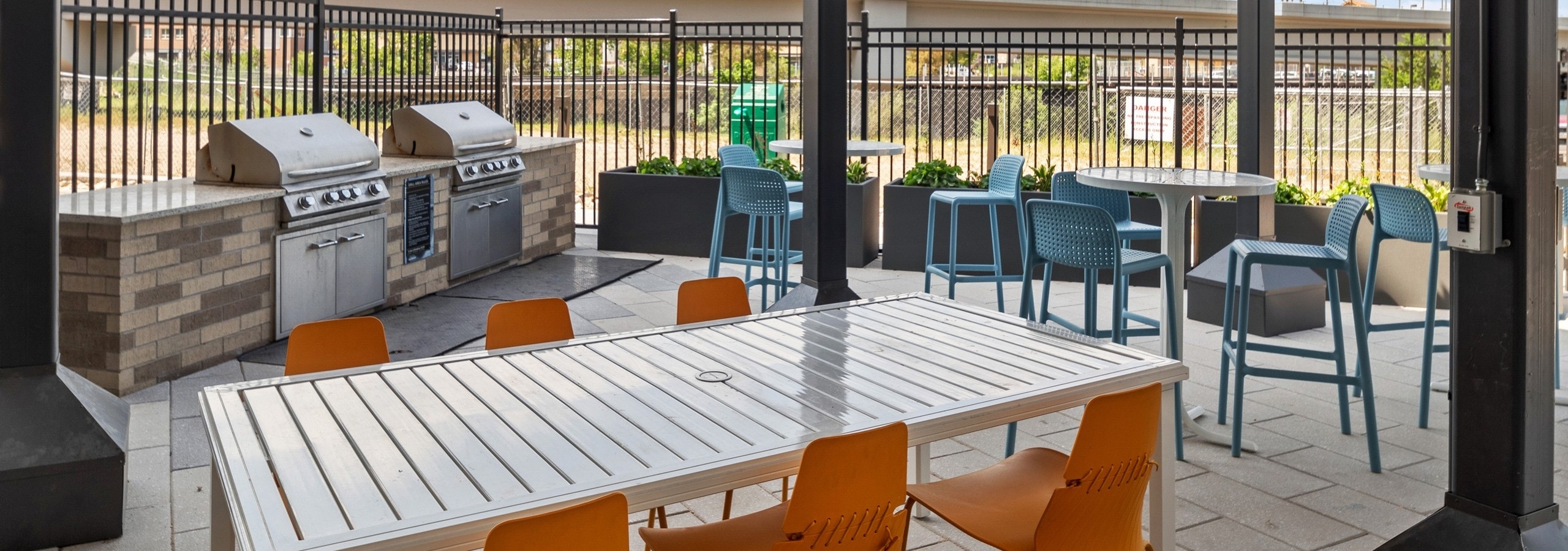 Grill station at AMLI RiNo apartments with 2 grills and white tables with orange and blue chairs surrounded by fence