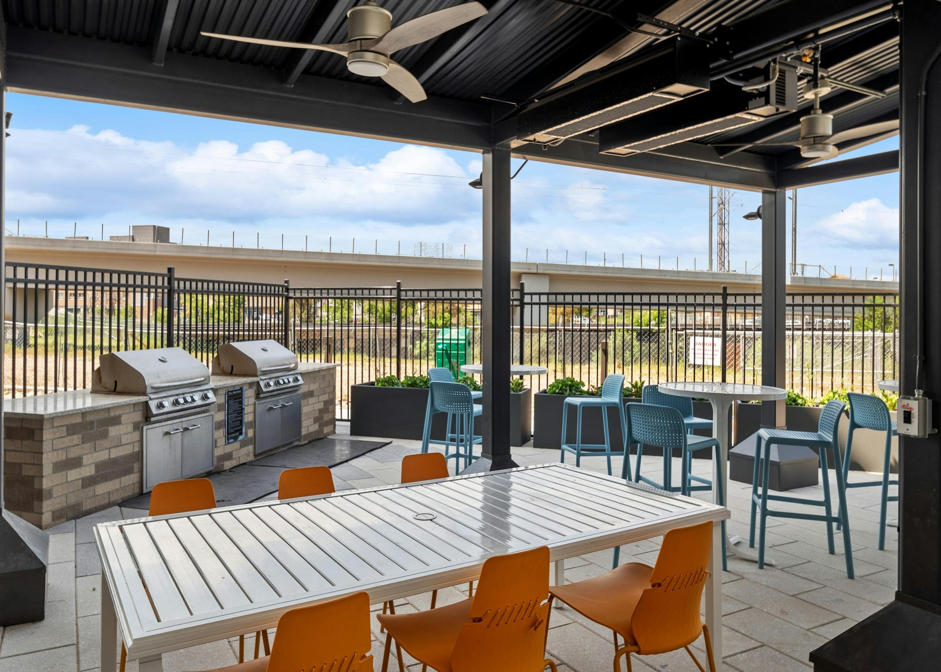 Grill station at AMLI RiNo apartments with 2 grills and white tables with orange and blue chairs surrounded by fence