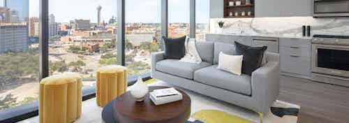 AMLI Fountain Place living room with gray couch and coffee table next to large wall of windows and light gray kitchen behind