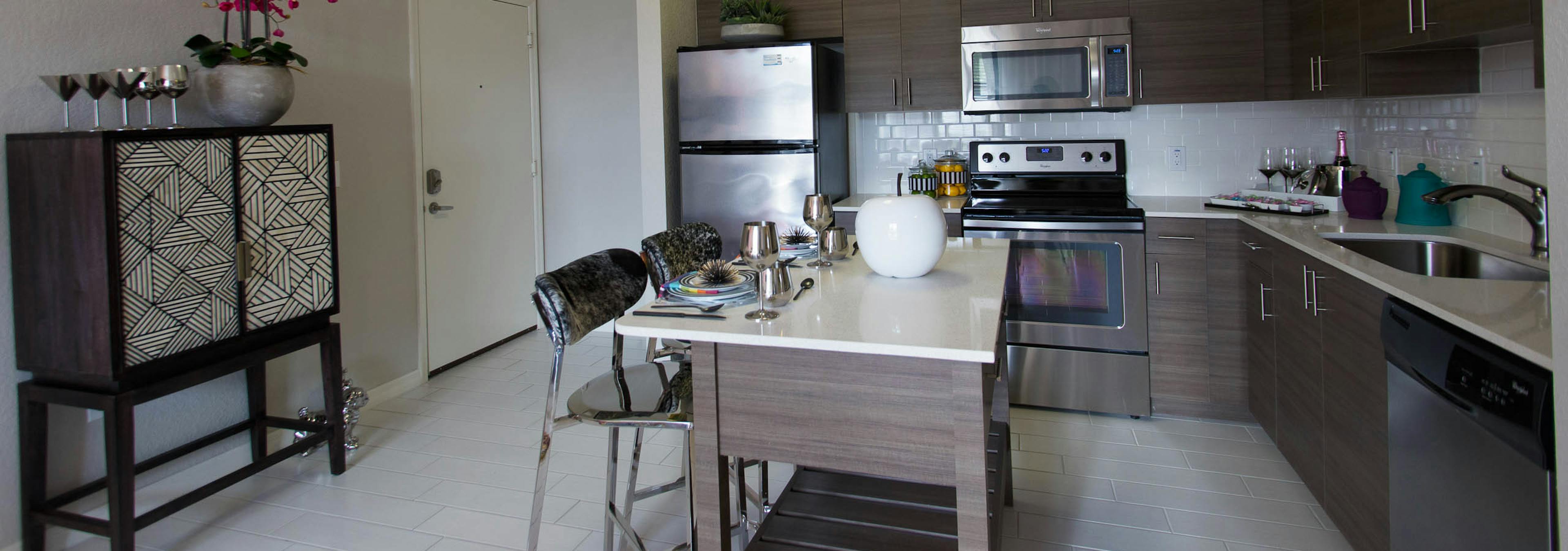  Interior view of AMLI Dadeland apartment island kitchen with stainless steel appliances and dark wood cabinetry