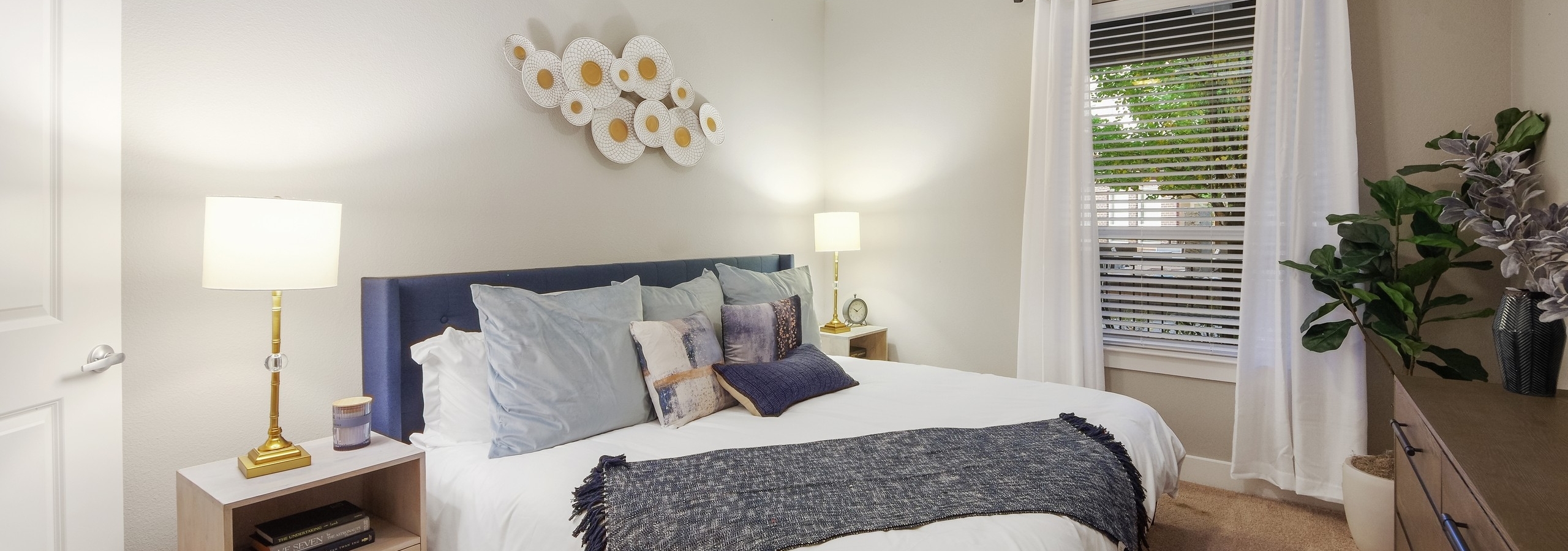 AMLI Riverfront Park apartment bedroom with light walls and carpeting featuring a spacious white bed with blue accents