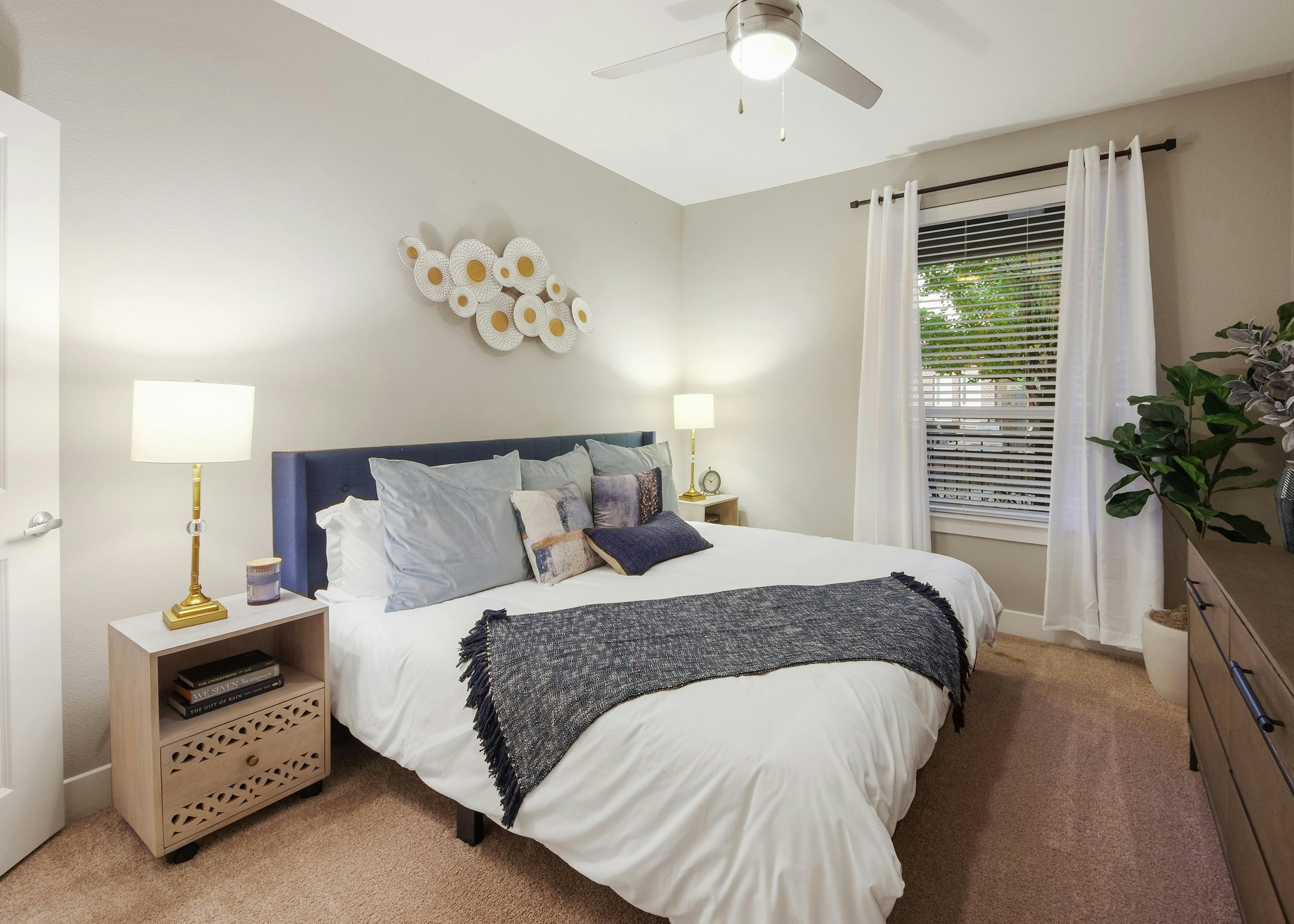 AMLI Riverfront Park apartment bedroom with light walls and carpeting featuring a spacious white bed with blue accents