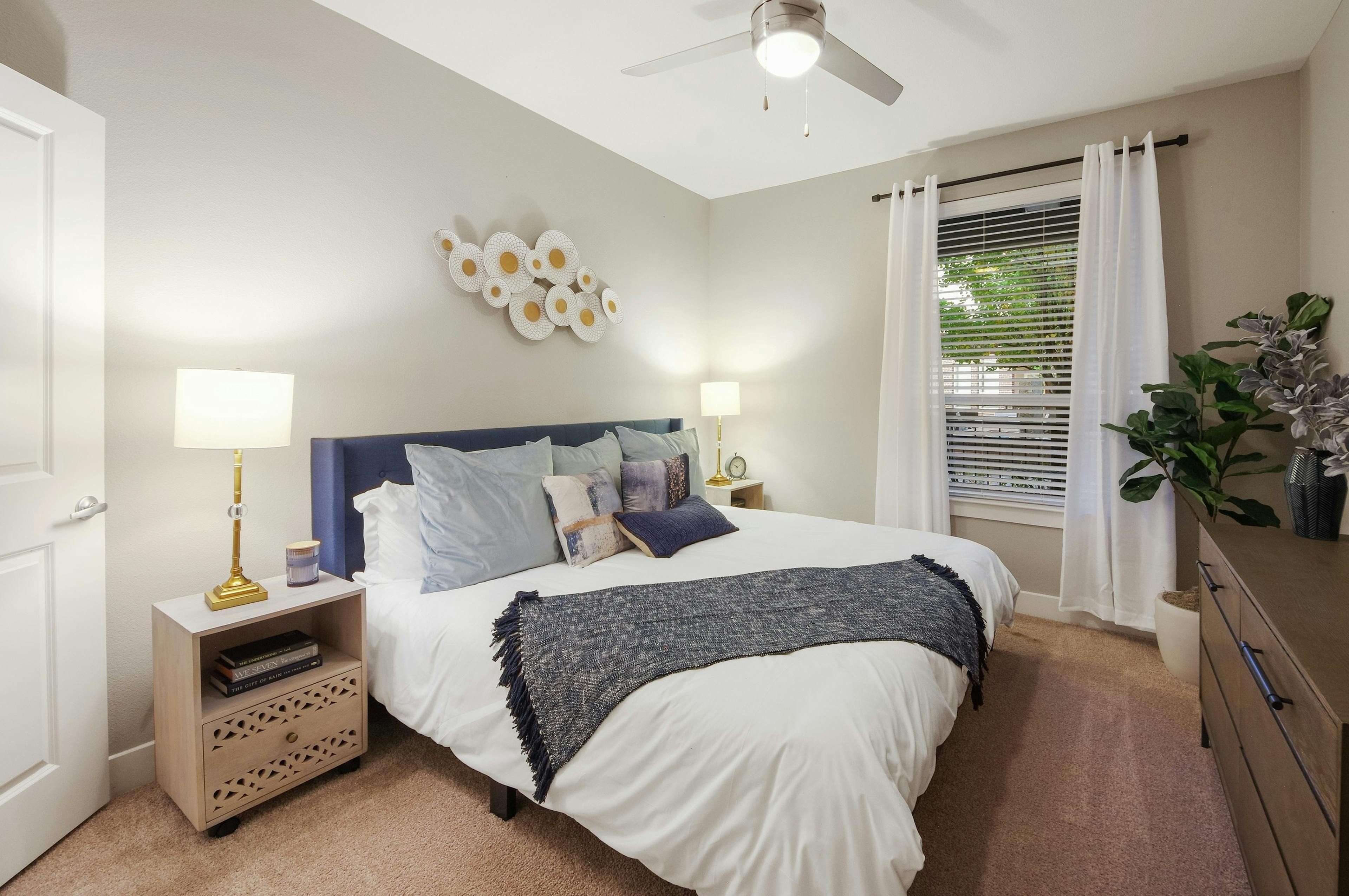 AMLI Riverfront Park apartment bedroom with light walls and carpeting featuring a spacious white bed with blue accents