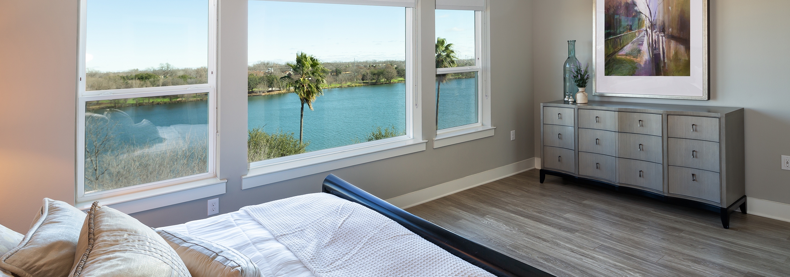 AMLI South Shore bedroom with long windows overlooking Lady Bird Lake and light hardwood with neutral walls and decor