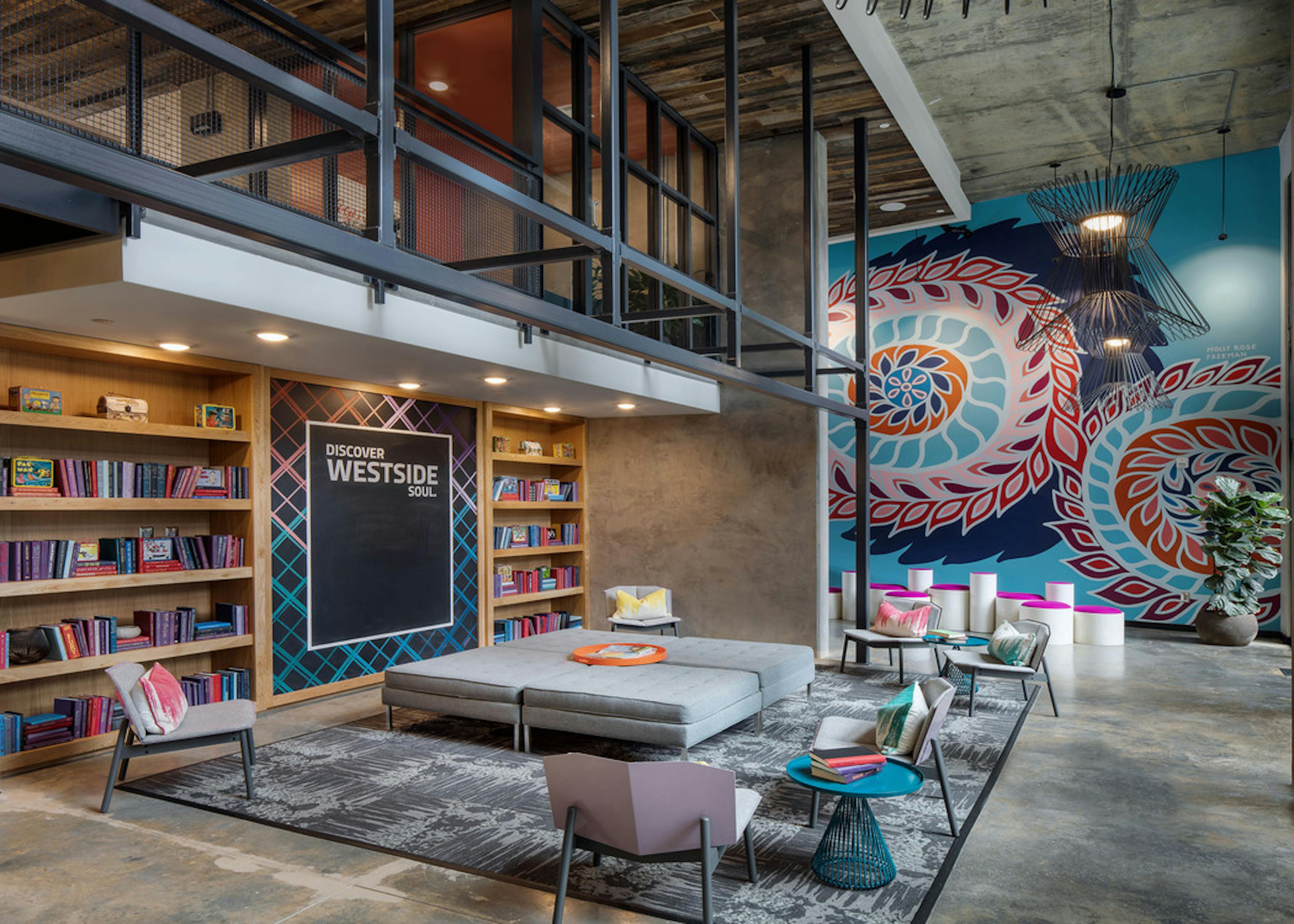 AMLI Westside library with long wooden shelf and concrete flooring with lounge seating and large colorful mural on back wall