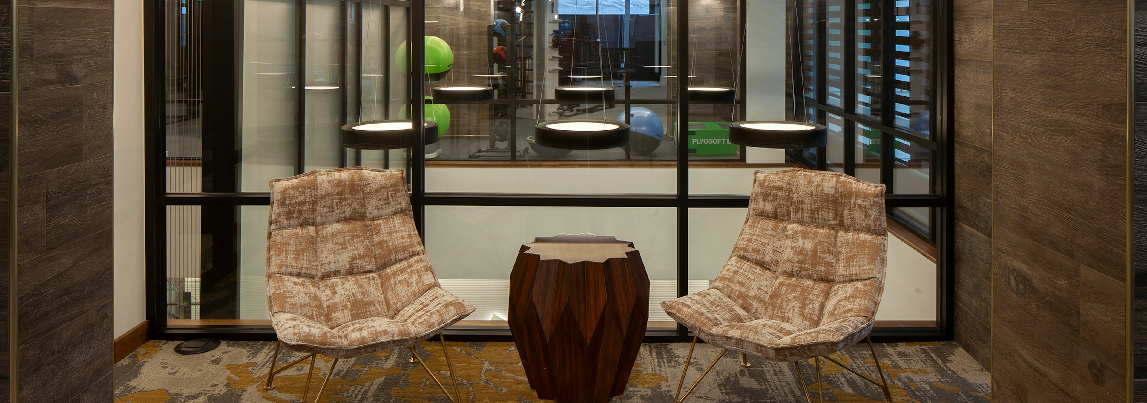 A clubhouse seating area at AMLI Riverfront Green apartments showcasing stylish chairs with an ottoman and wood panel walls