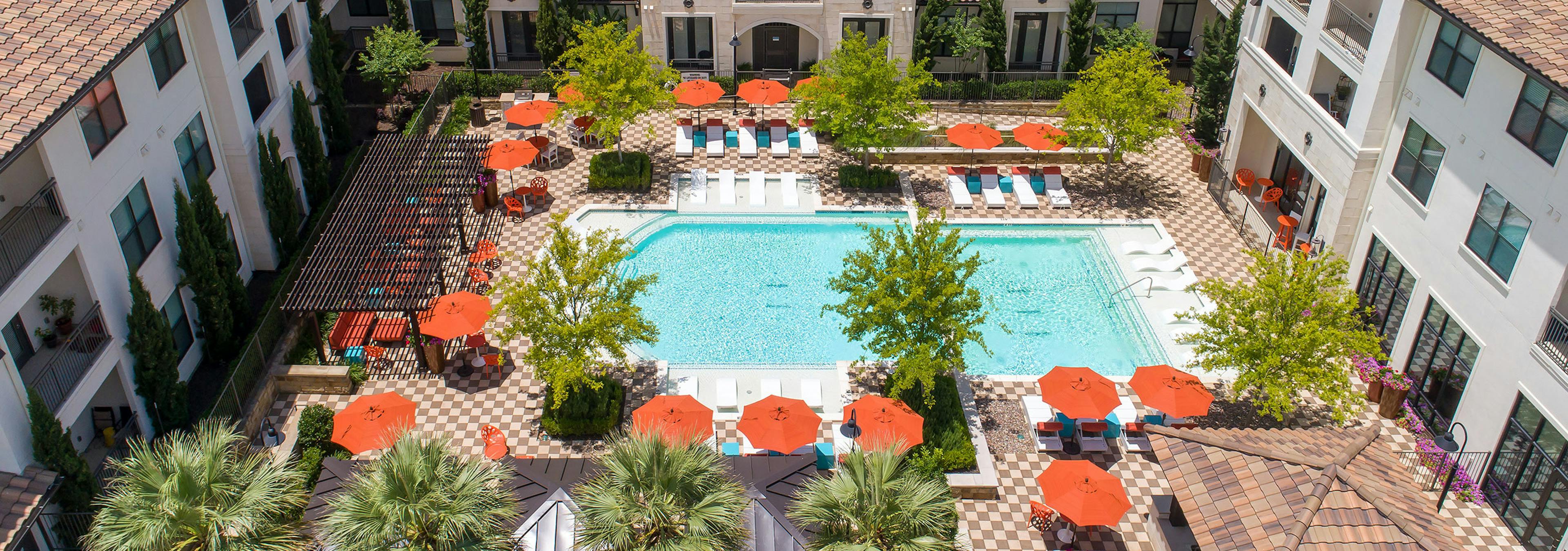 Sunny daytime aerial view of the pool at AMLI on Riverside with vibrant trees and orange umbrellas lining the poolside 