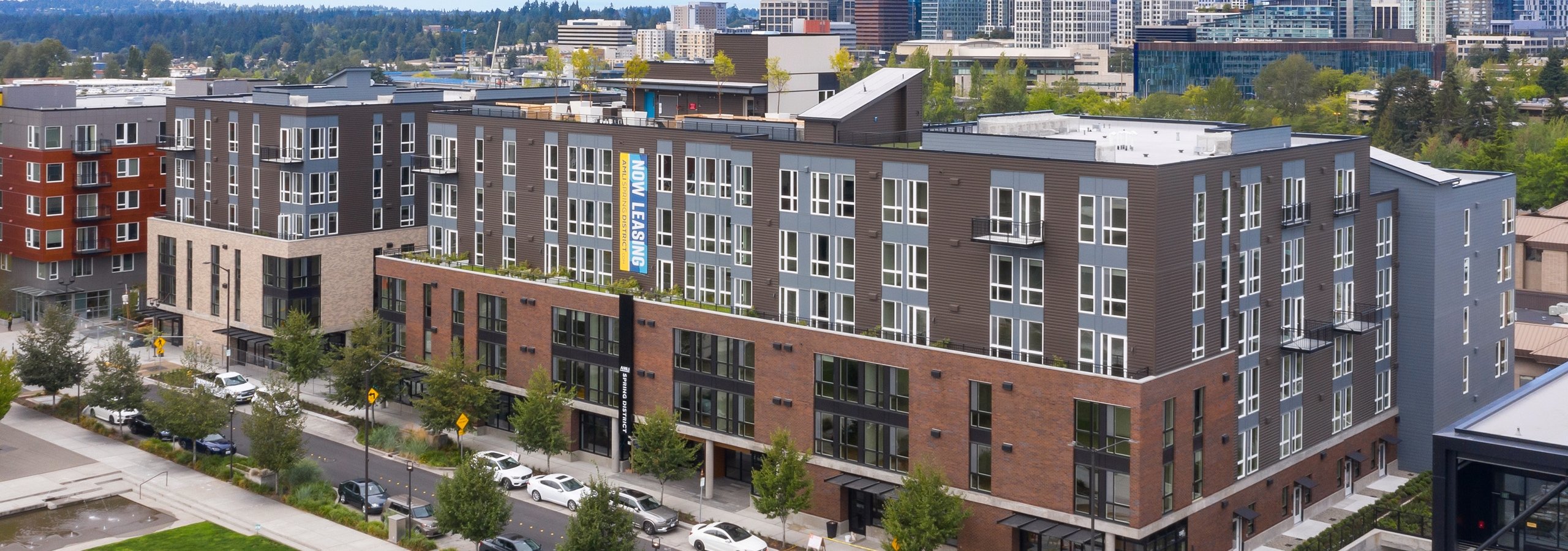 Aerial view of AMLI Spring  District apartment building with rooftop deck above and street with cars and skyline in rear
