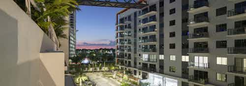 Dusk exterior view of AMLI Midtown Miami apartment buildings with balconies and connecting bridge and lush landscaping below