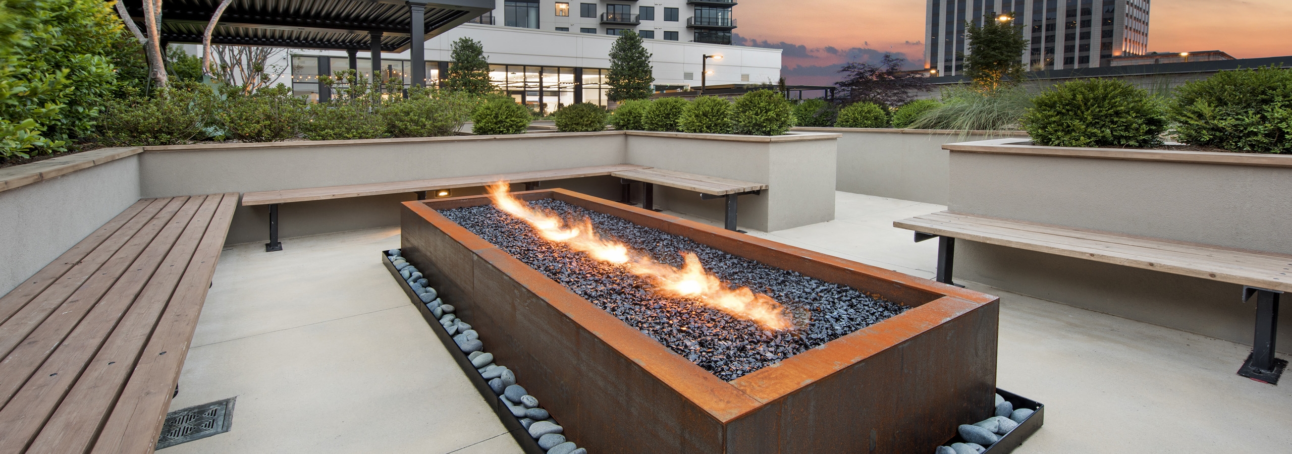 Evening view of outside seating area at AMLI Lenox with lit rectangular fireplace surrounded by brown benches for seating
