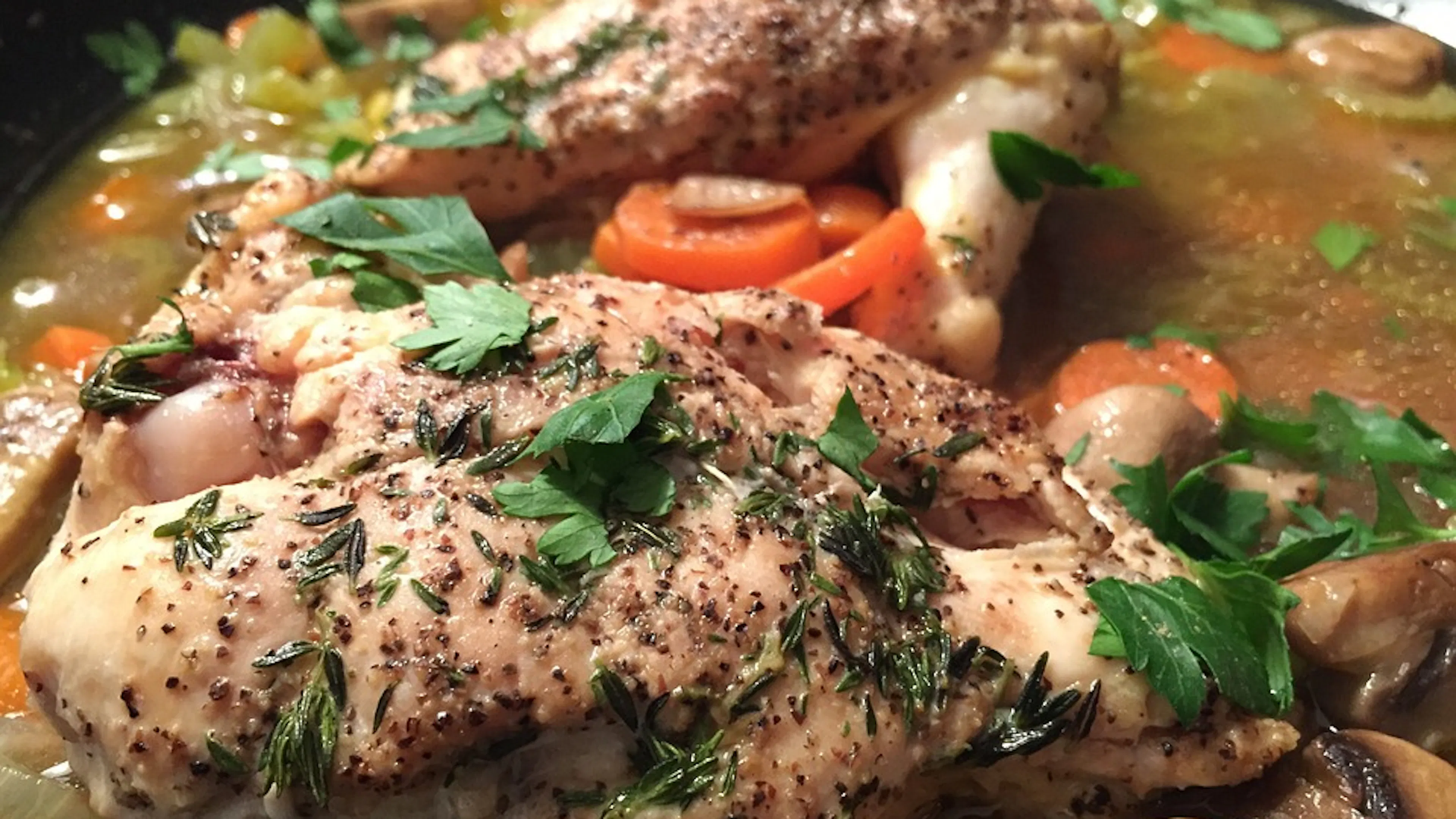 A chicken breast in a pan with tomatoes and mushrooms topped with cilantro