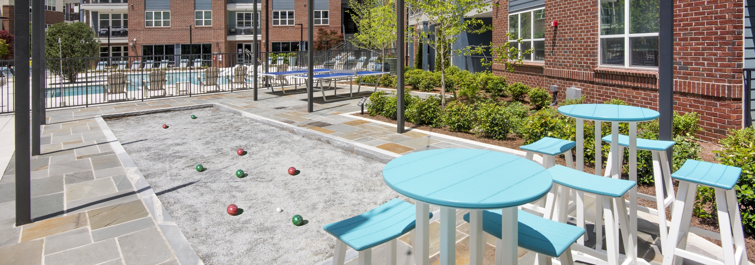 Daytime view of AMLI Decatur with bocce ball court next to high top teal tables and stools overlooking pool and building