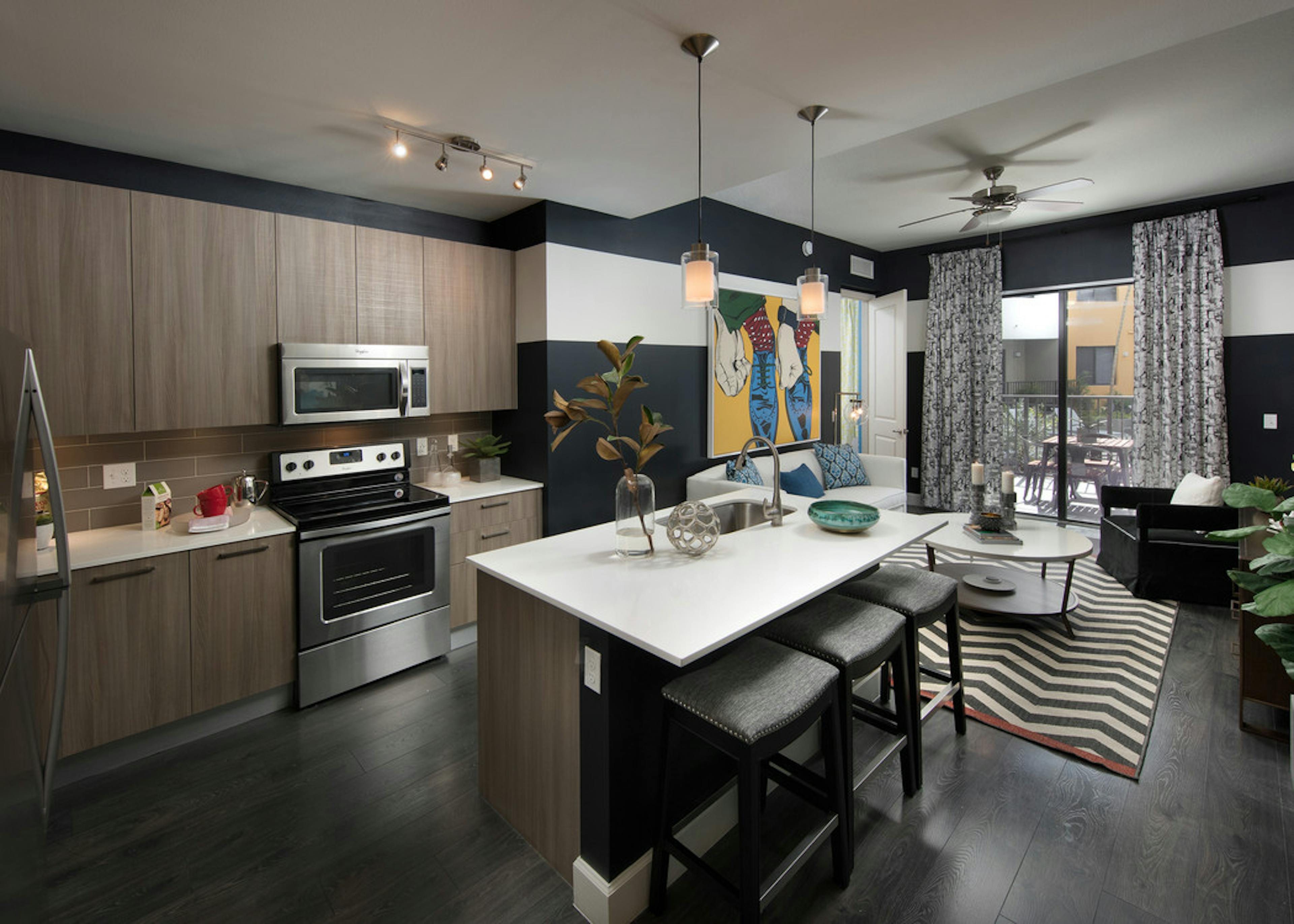 AMLI 8800 apartment with island kitchen with stools, stainless steel appliances, wood cabinetry and peek into living area 